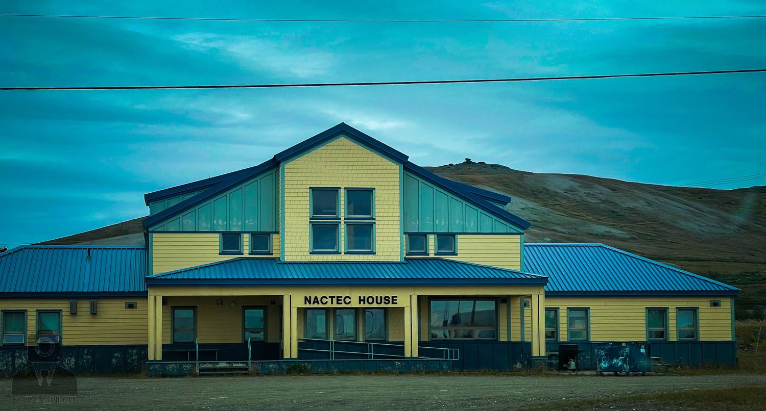 Row of yellow buildings with blue trim under dramatic sky in rural setting.