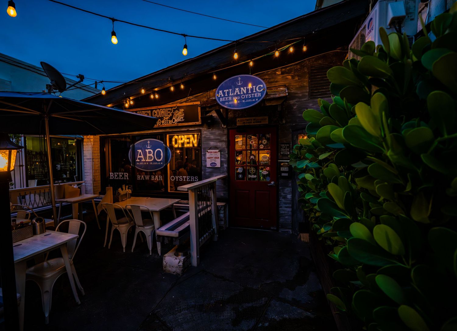 Outdoor dining area with string lights and restaurant signage at night.