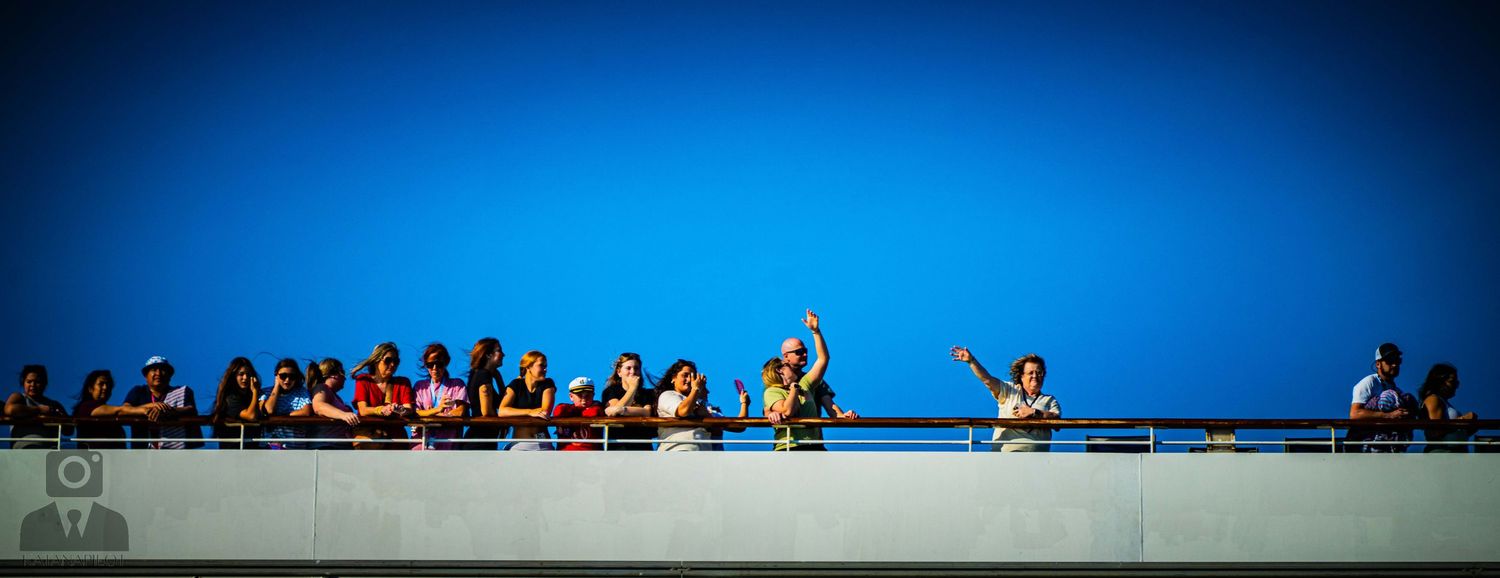Silhouetted crowd of people standing against vibrant blue sky during sunset or sunrise at a stadium event.