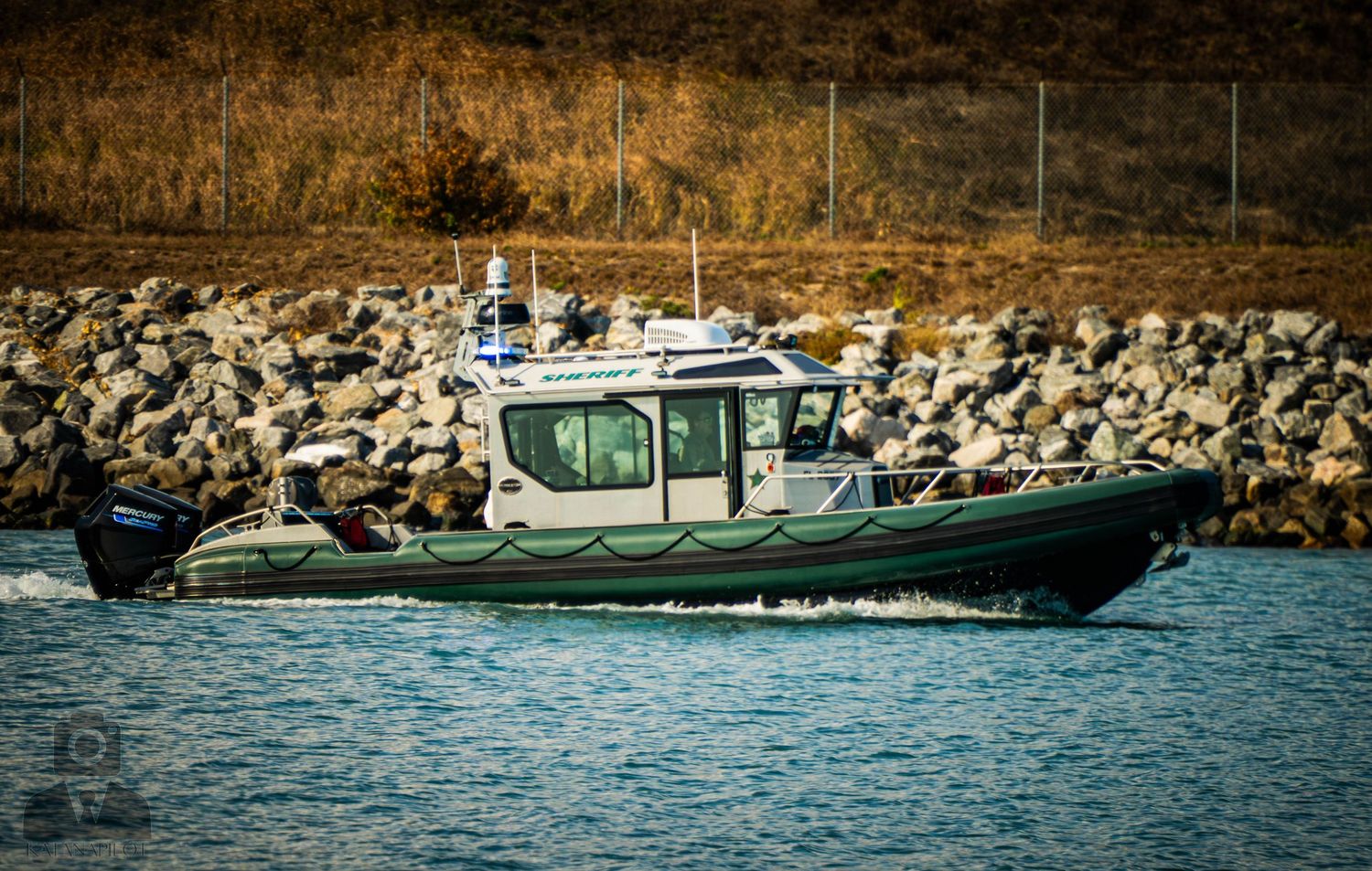 Luxury boats and yachts anchored near a rocky shoreline with calm blue waters on a sunny day.