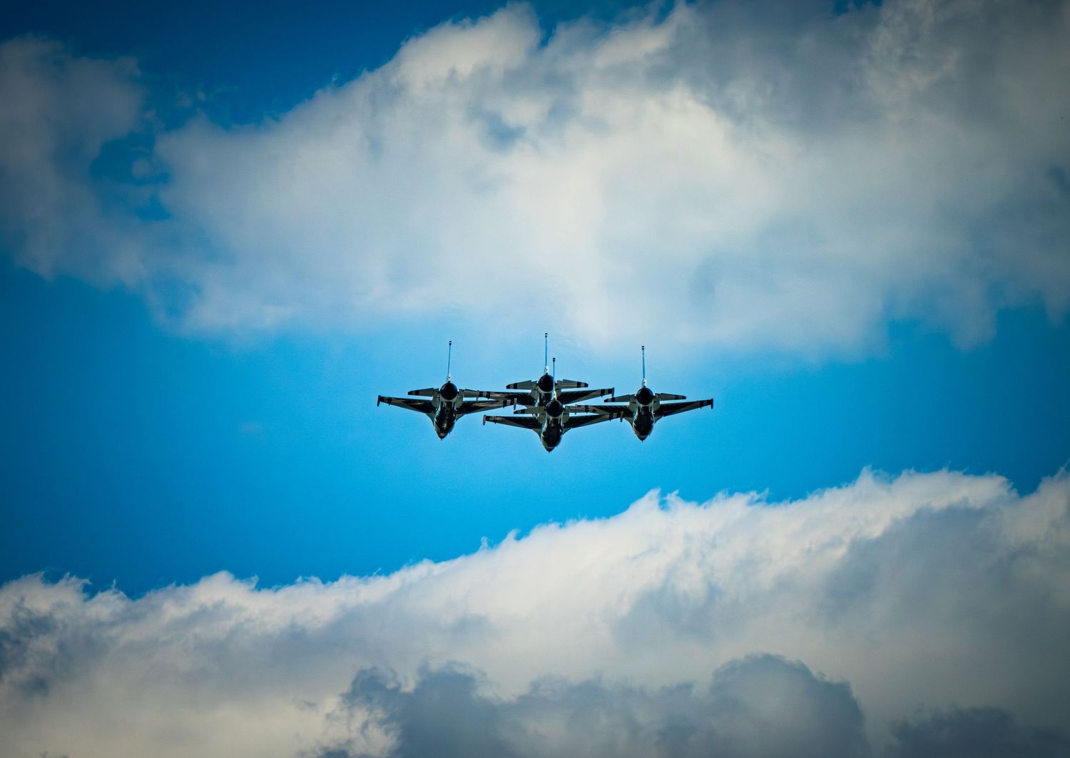 Two military jets flying in tight formation against a vivid blue sky with scattered white clouds.