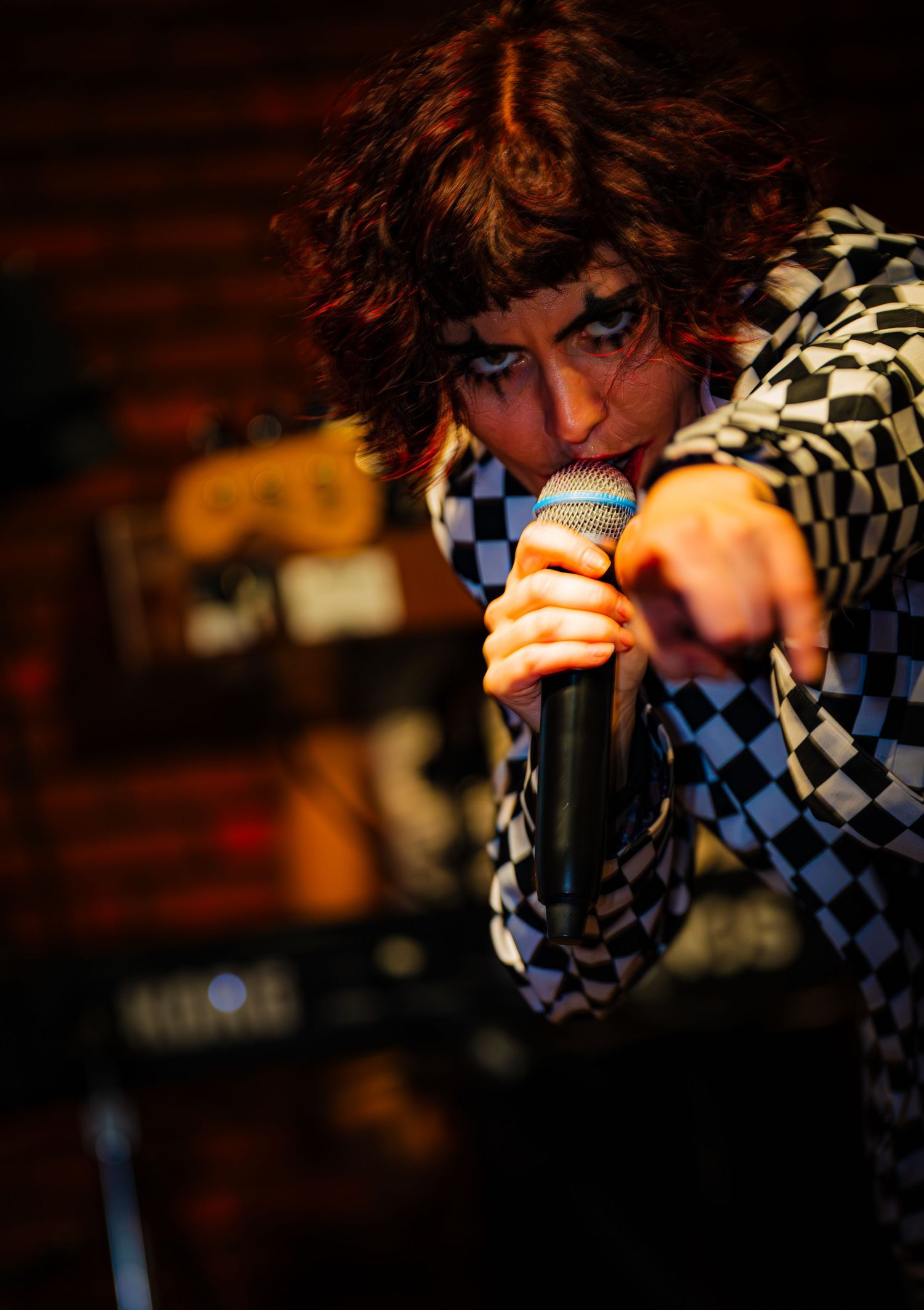 Singer in checkered outfit performs intensely at microphone during concert.