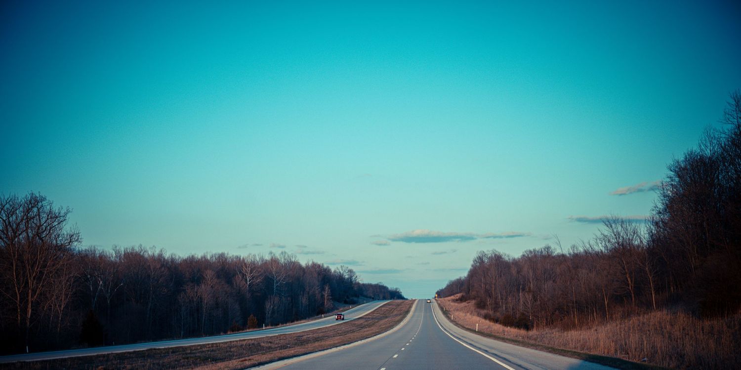 Empty highway stretching into the distance under a bright blue sky.
