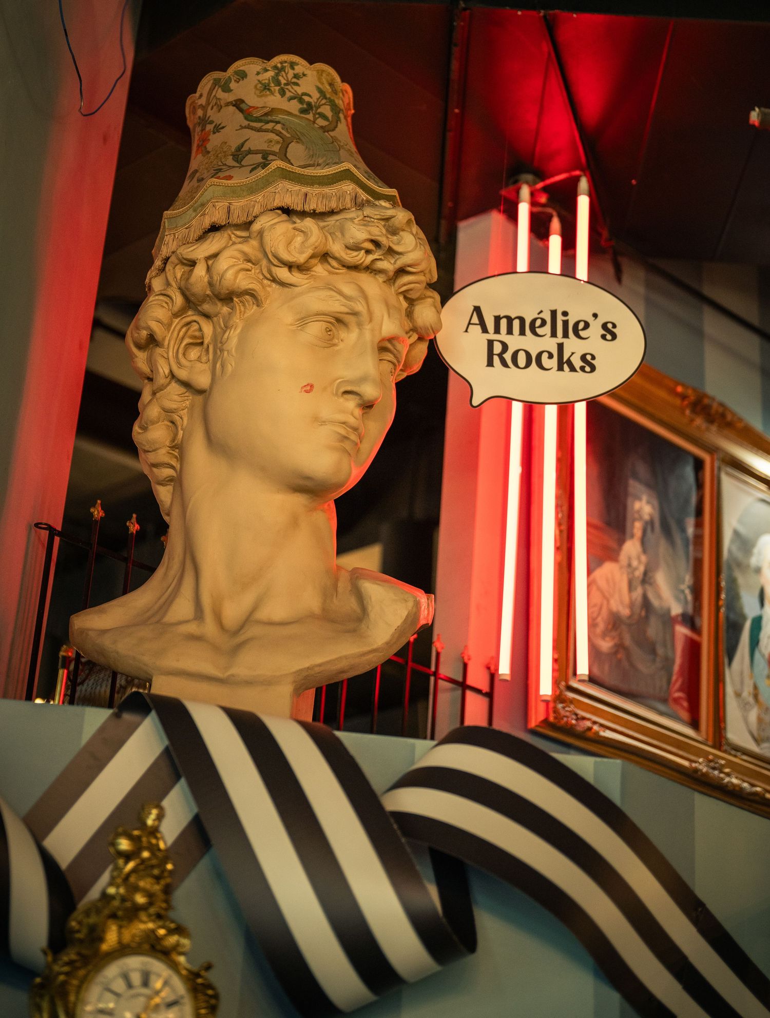 Classical marble bust sculpture with striped background and red lighting in a restaurant setting.