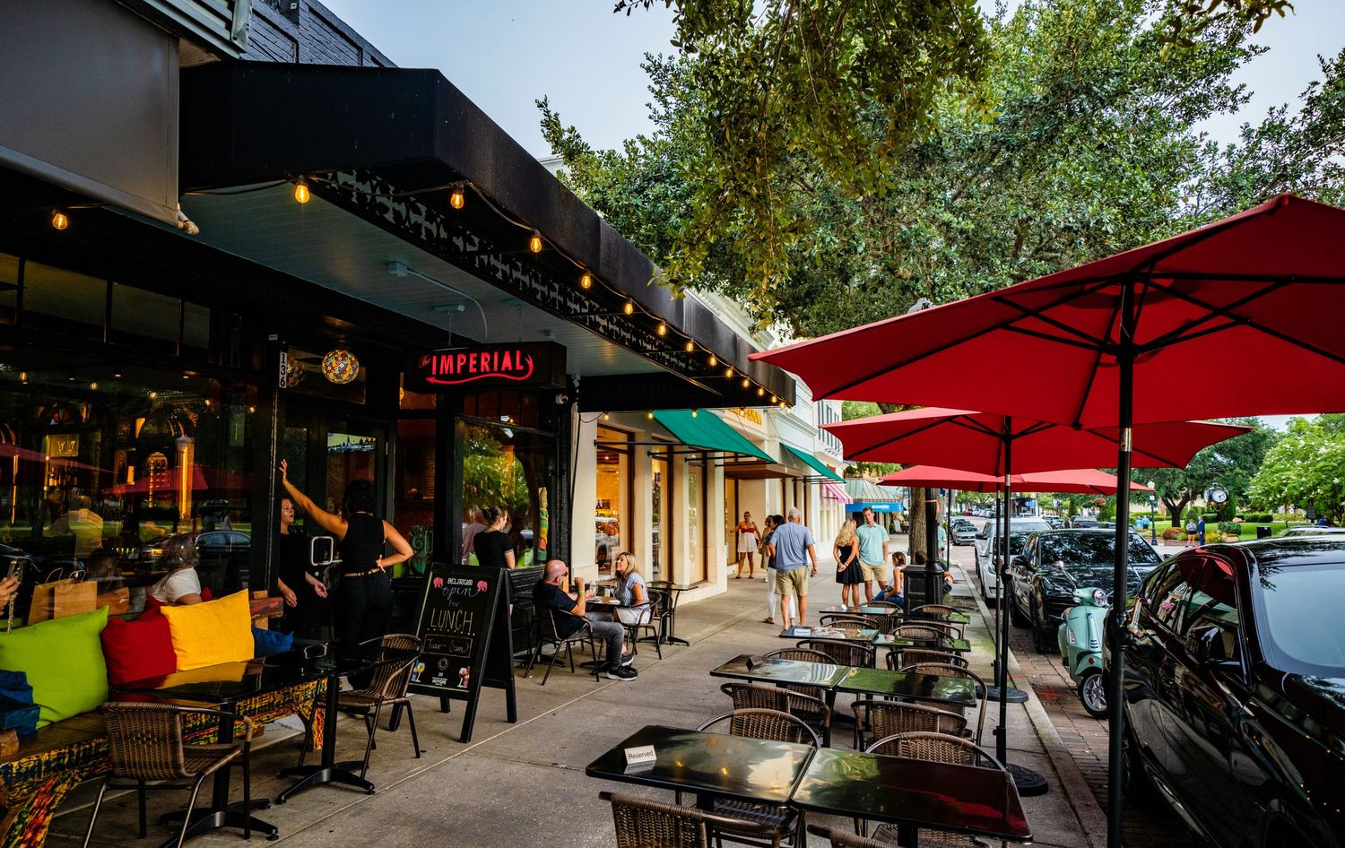 Outdoor dining area with red umbrellas and seating along a covered walkway.