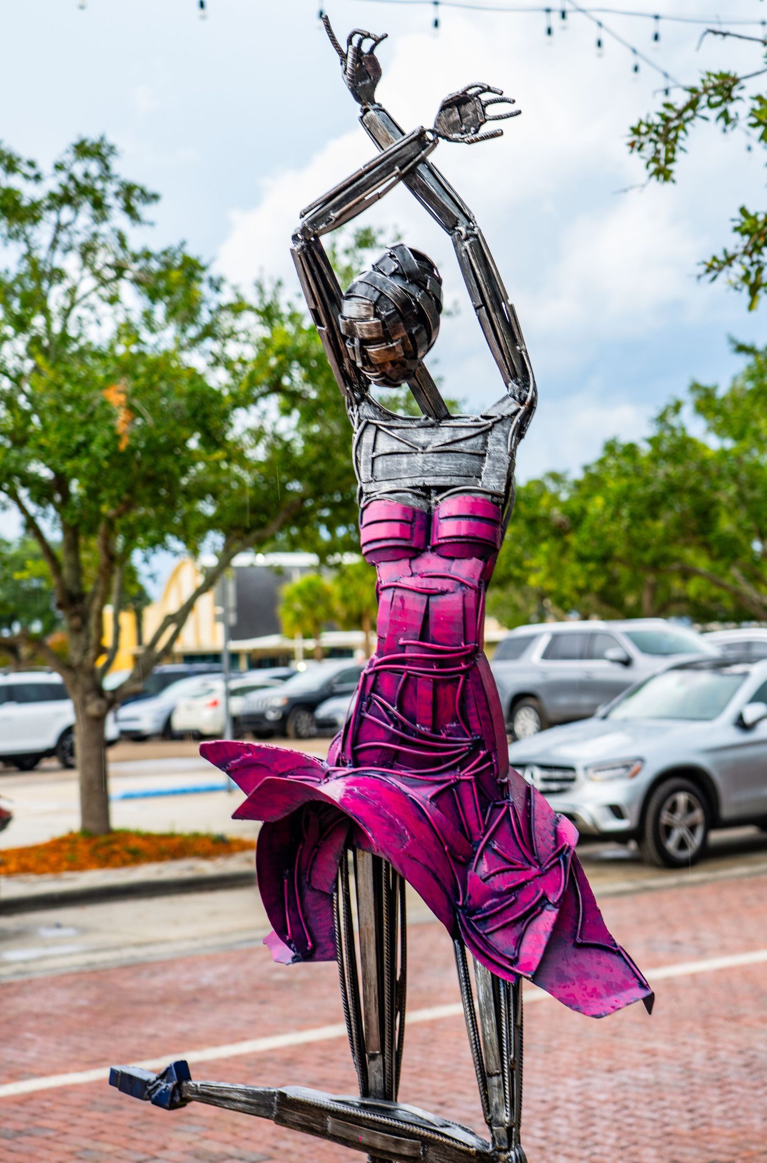 Purple metal sculpture of dancing figures displayed in downtown plaza.