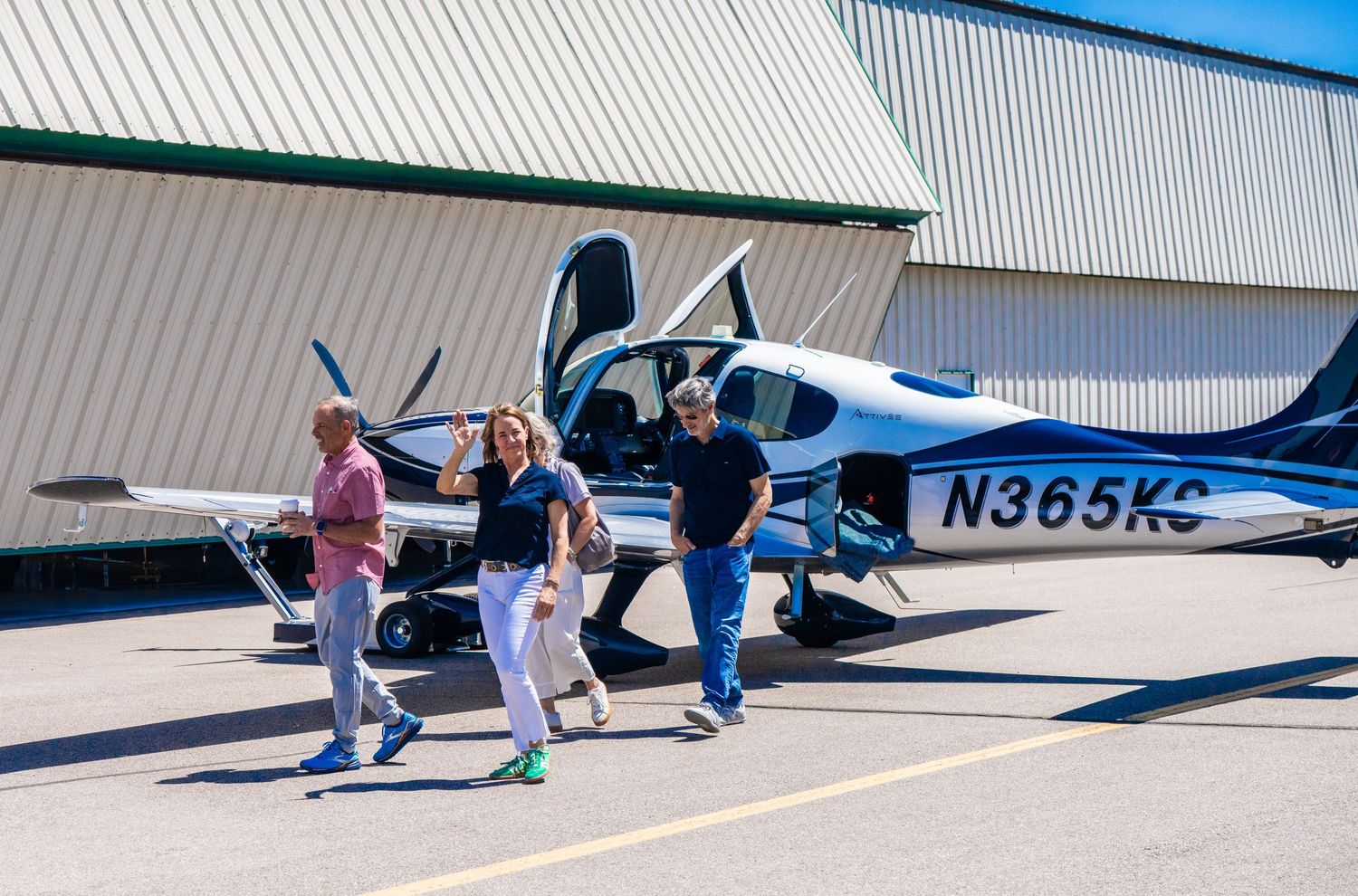 Aircraft parked outside hangars with people walking around on sunny day.
