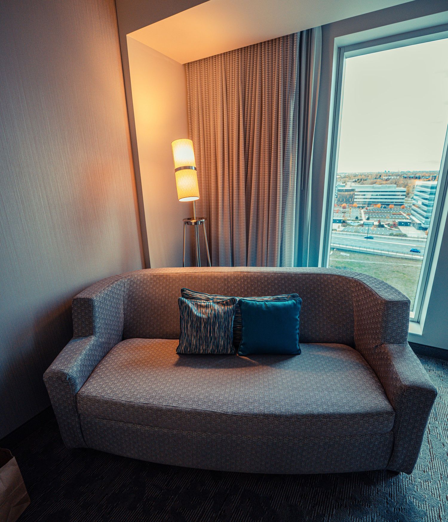 Contemporary hotel room daybed with harbor view through large windows.