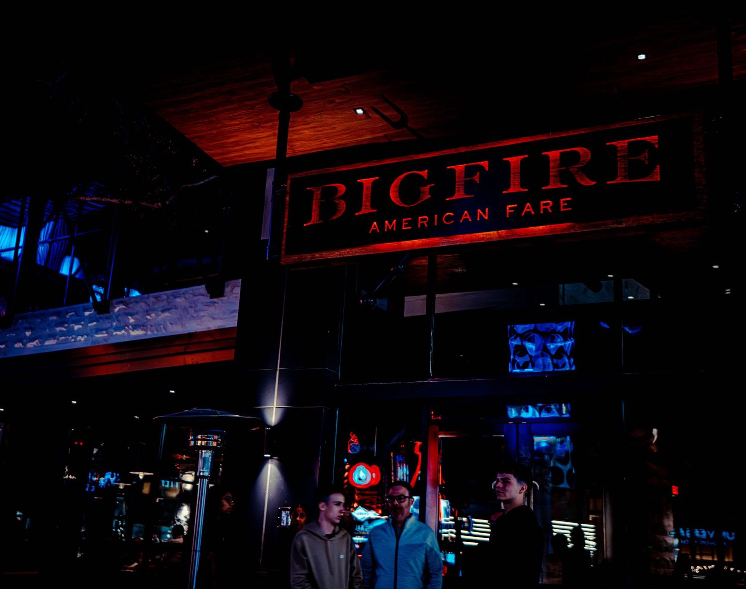 Dark nightclub interior with neon lighting and silhouettes of people at a bar counter.