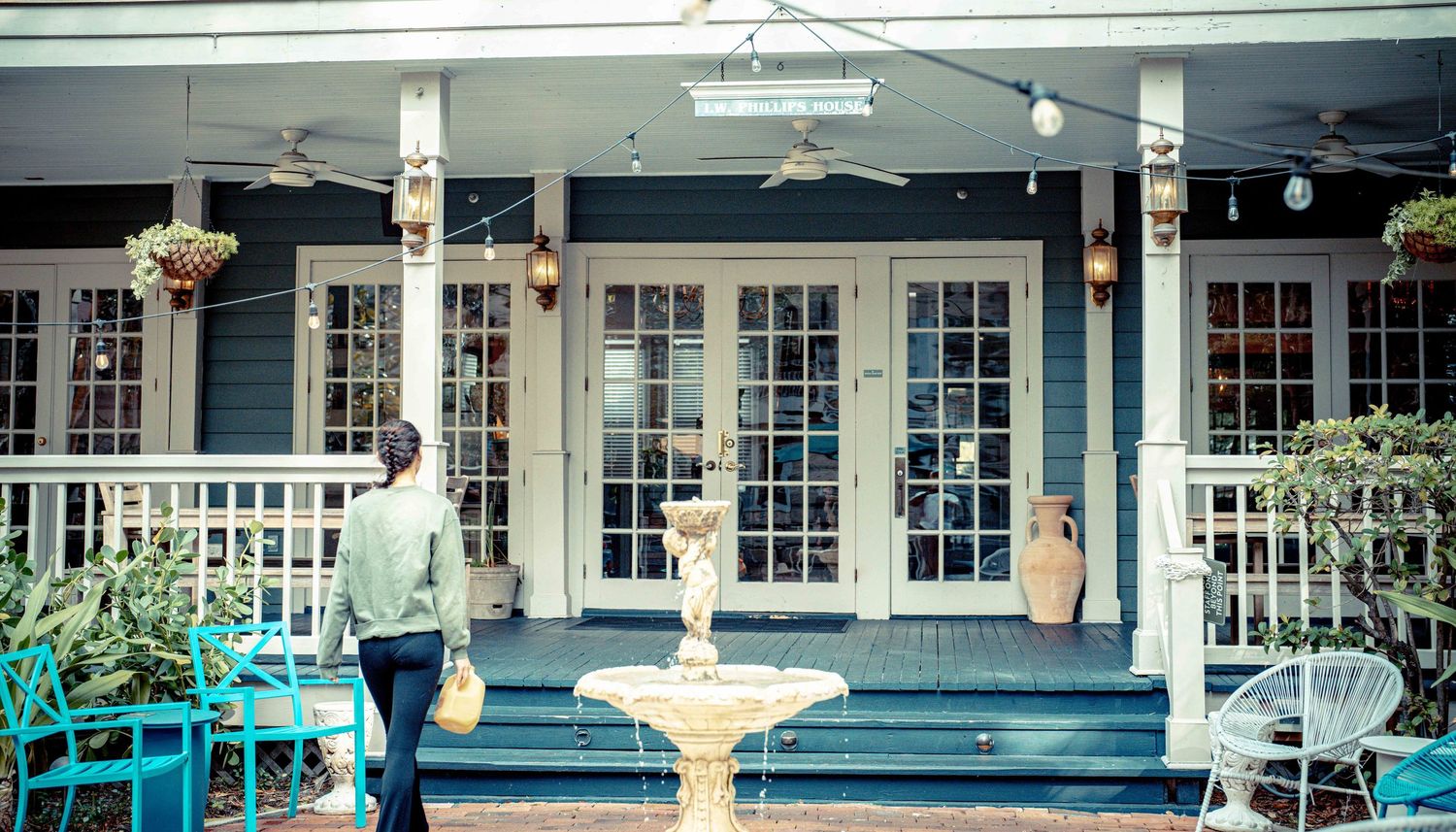 A charming blue and white porch with French doors, white railing, and a decorative fountain in front of a historic home.