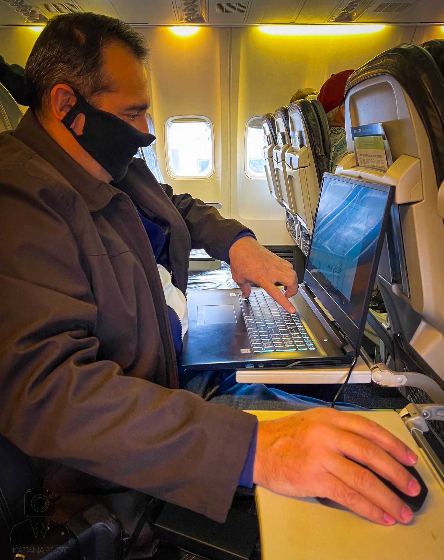 Person working on laptop computer while seated in airplane cabin.