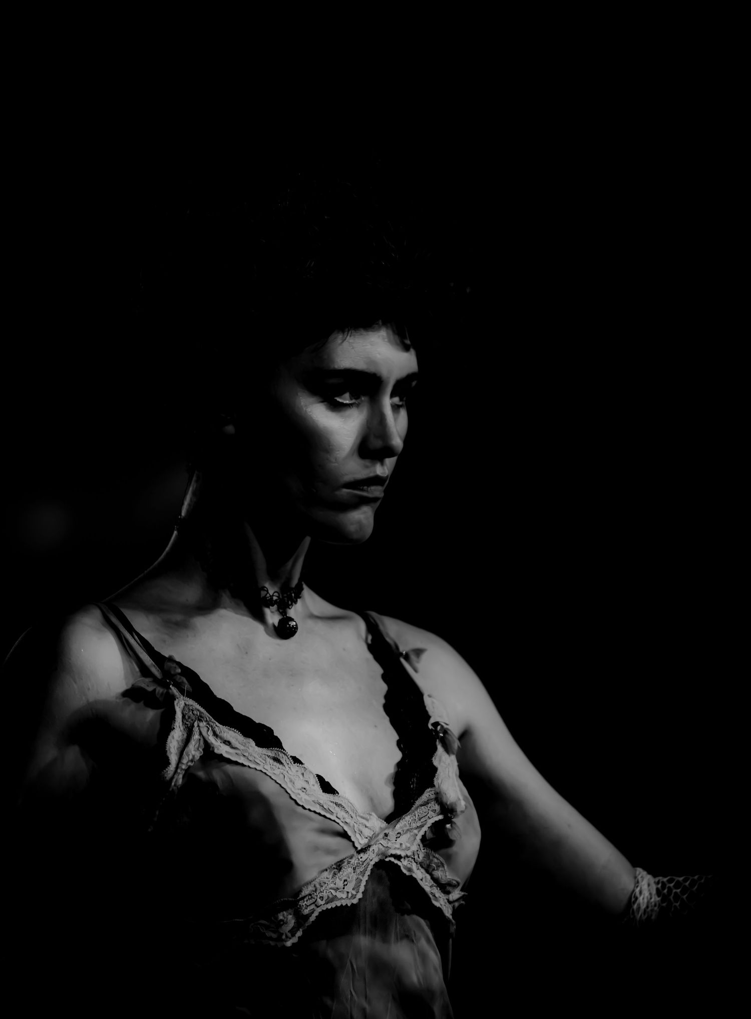 Dramatic black and white portrait of a woman in lace lingerie, lit with moody chiaroscuro lighting against dark background.