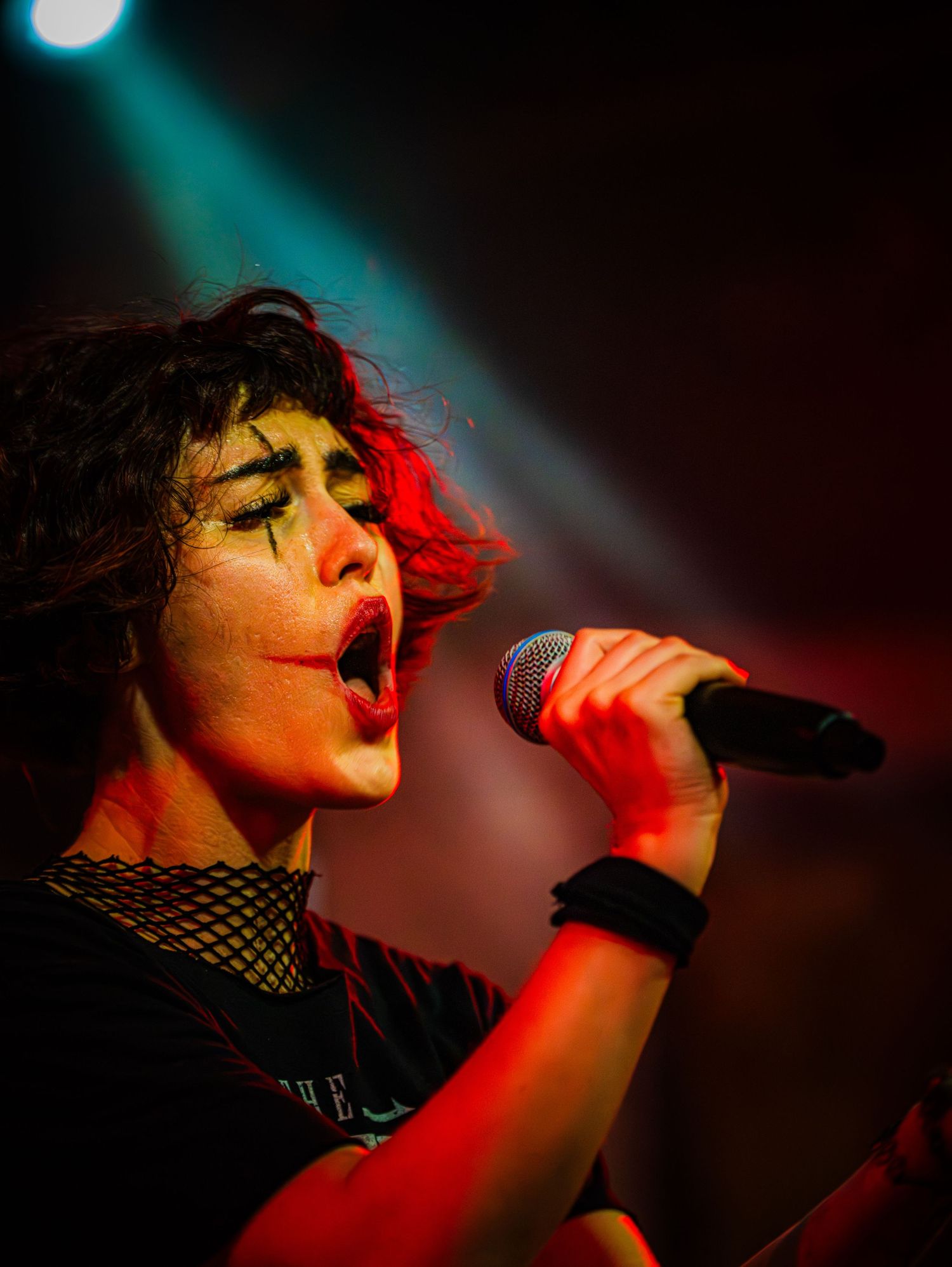 Female rock singer performing on stage under red and green lights, passionately singing into a microphone.