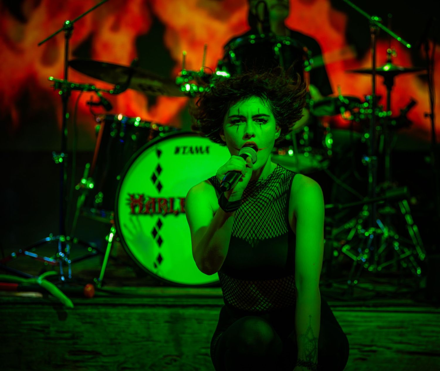 Drummer performing on stage with dramatic green and red lighting effects.