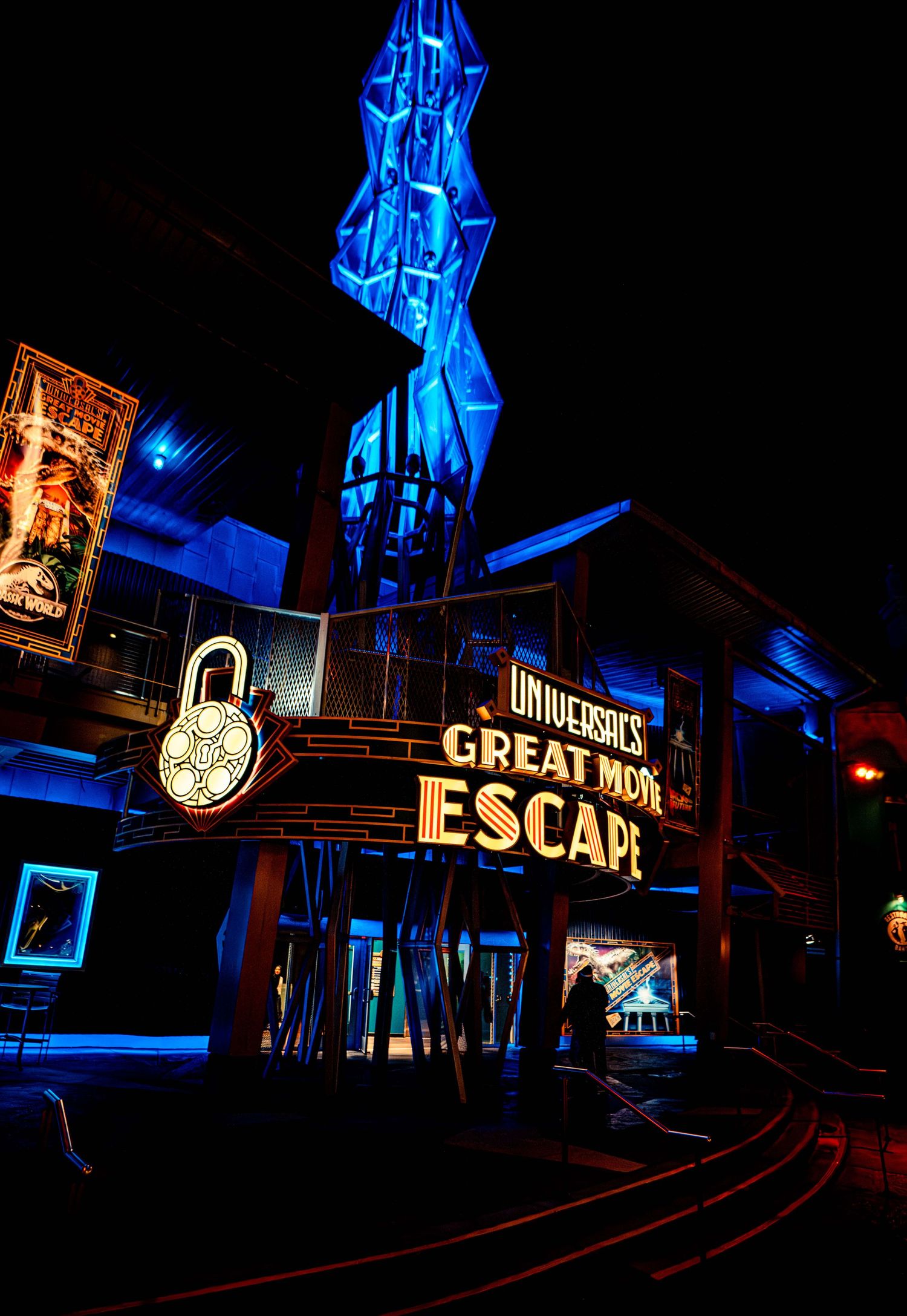 Illuminated blue neon sign for Universal's Great Movie Escape attraction at night with glowing lock symbol.