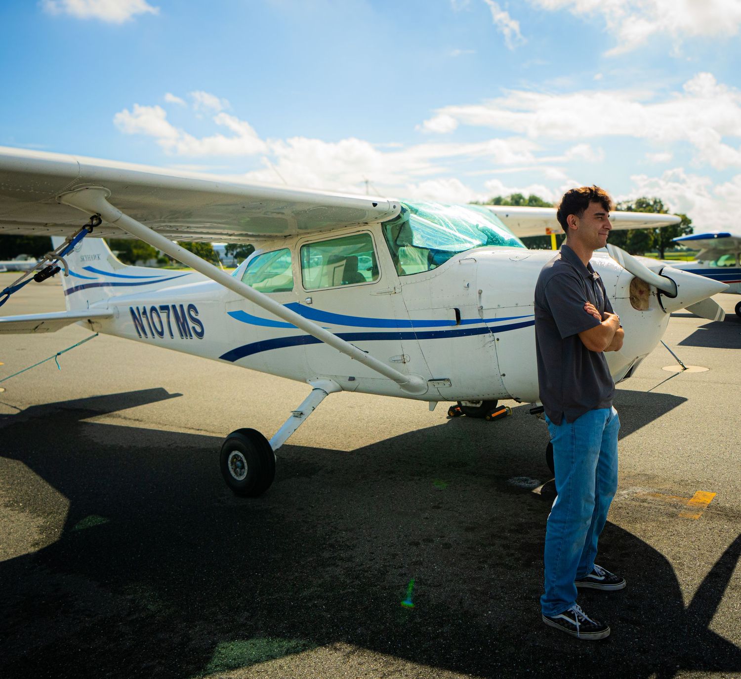 Young man standing beside a small Cessna plane with tail number N107MS on a sunny airport tarmac.