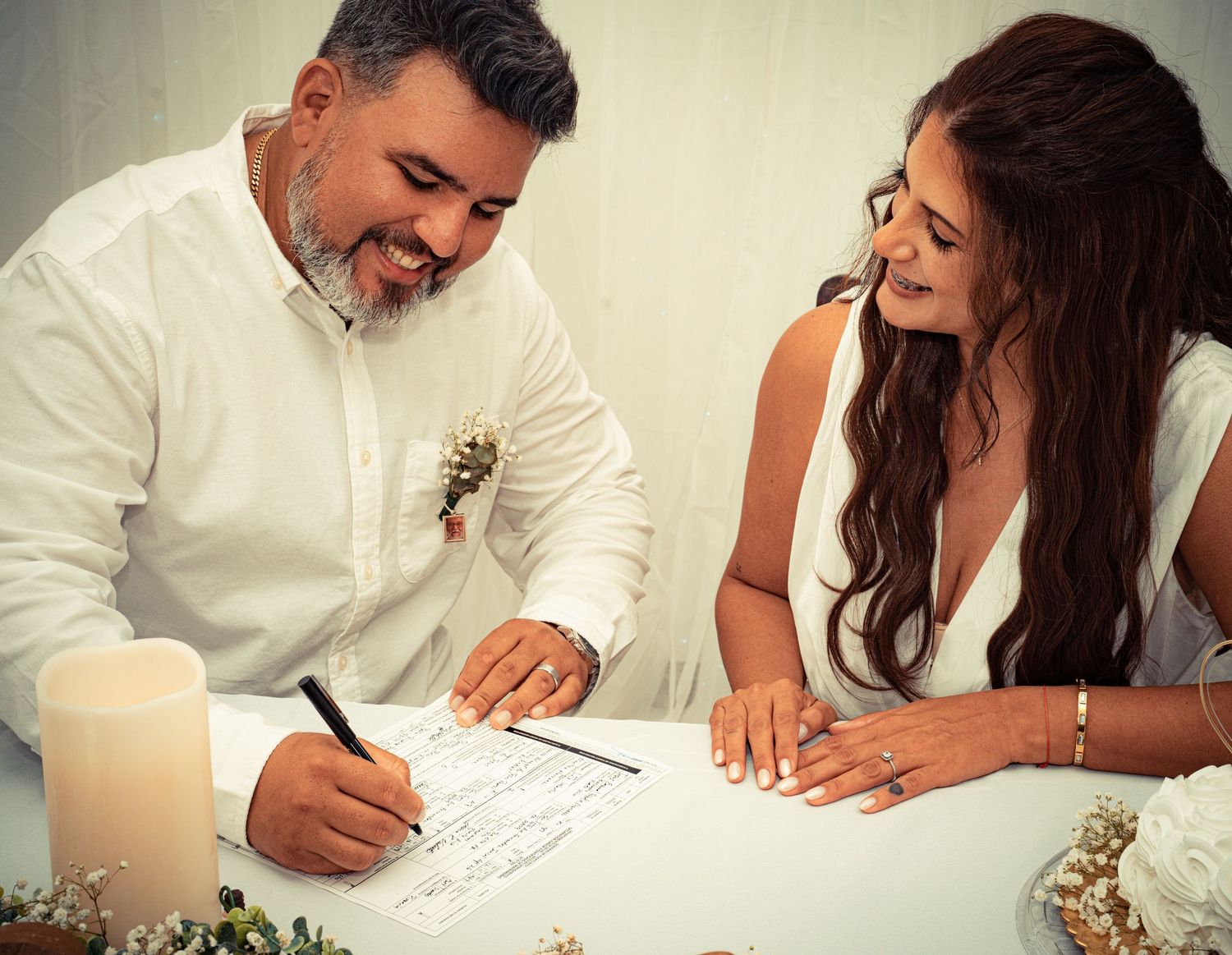 A couple signs their marriage license at a wedding ceremony while smiling and sharing a special moment together.