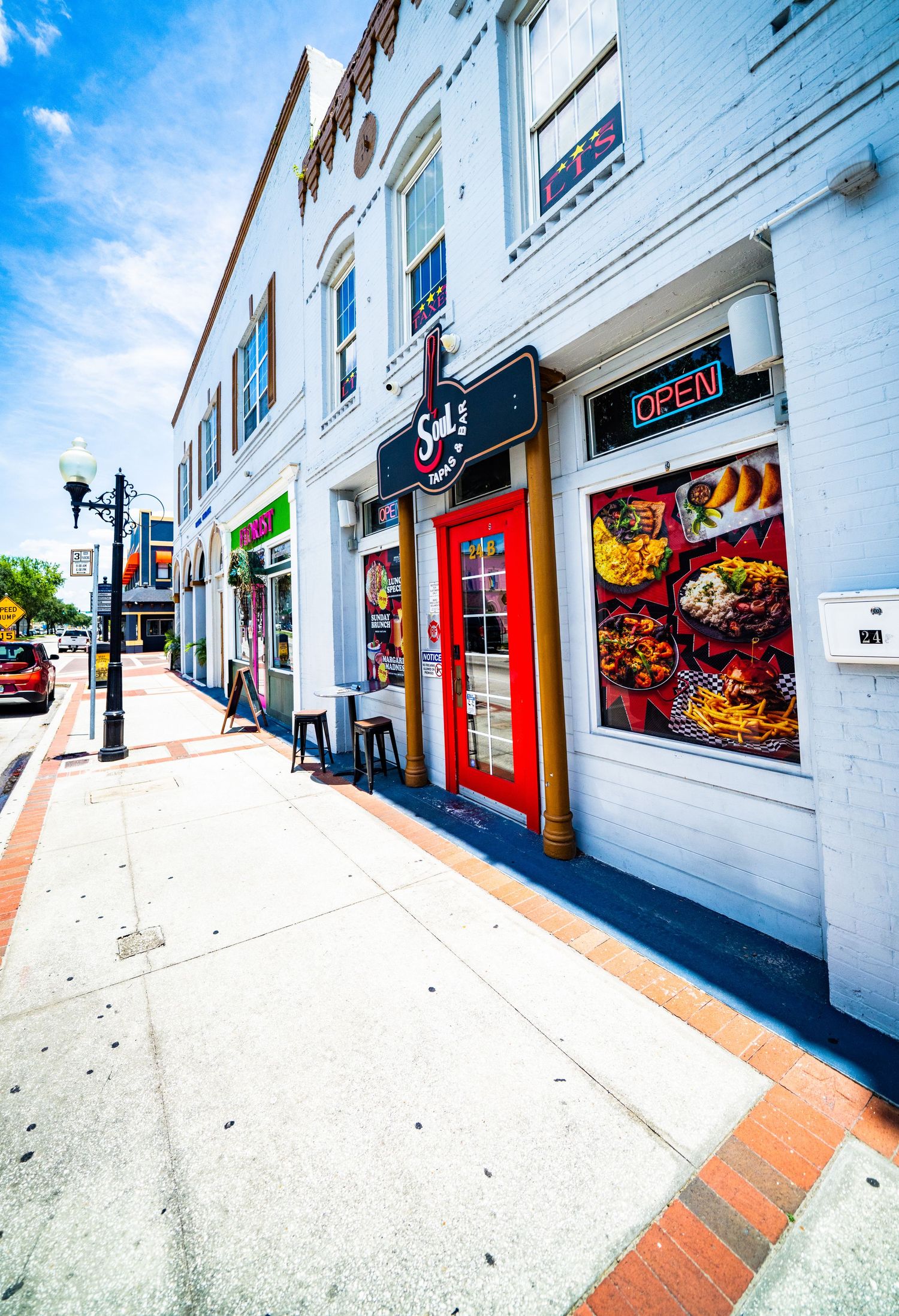 Colorful storefronts with red doors and vibrant window displays line a downtown sidewalk on a sunny day.