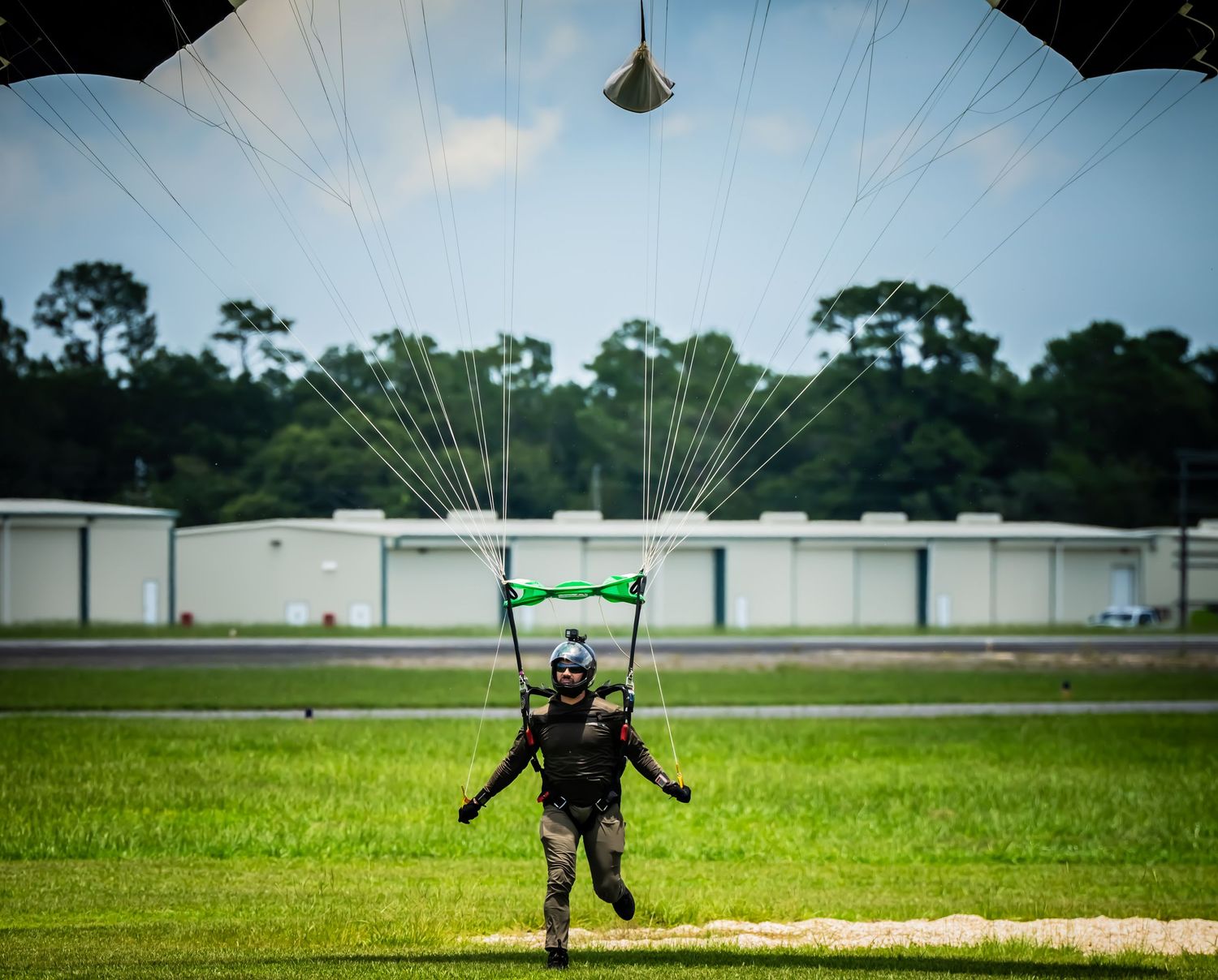 Parachutist landing sequence on a grassy airfield with buildings in the background.