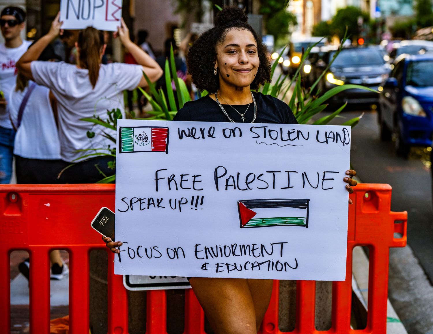 Protester holding sign supporting Palestine at street demonstration with red barrier.