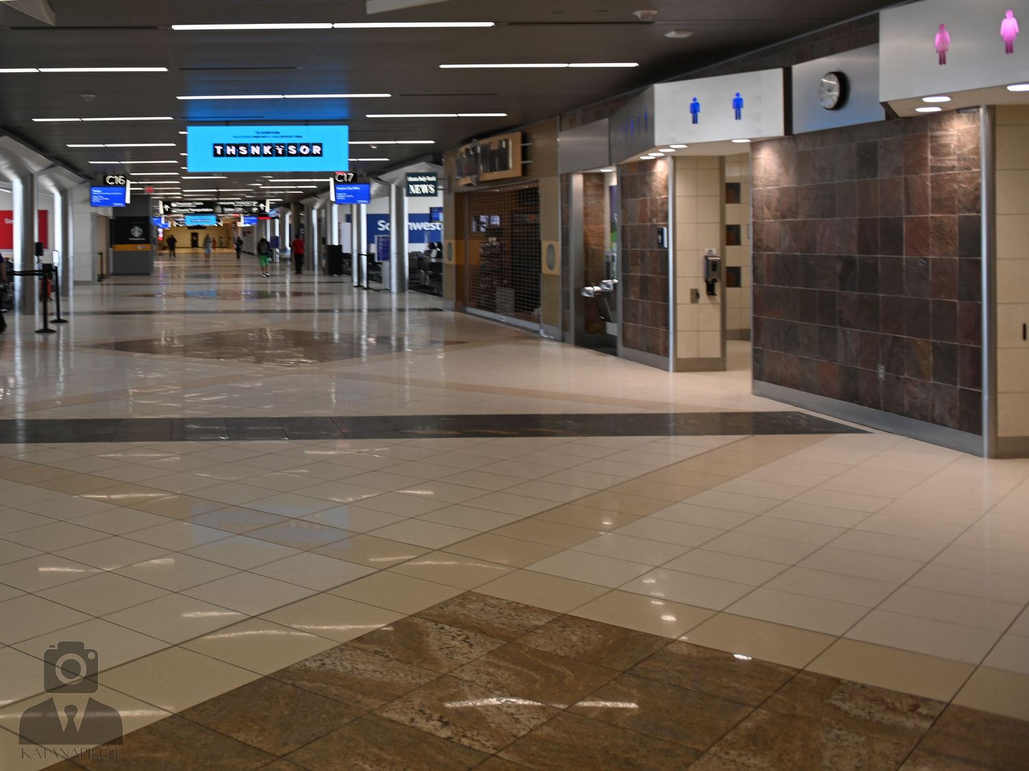 Empty mall corridor with tiled floor and illuminated storefront signs.