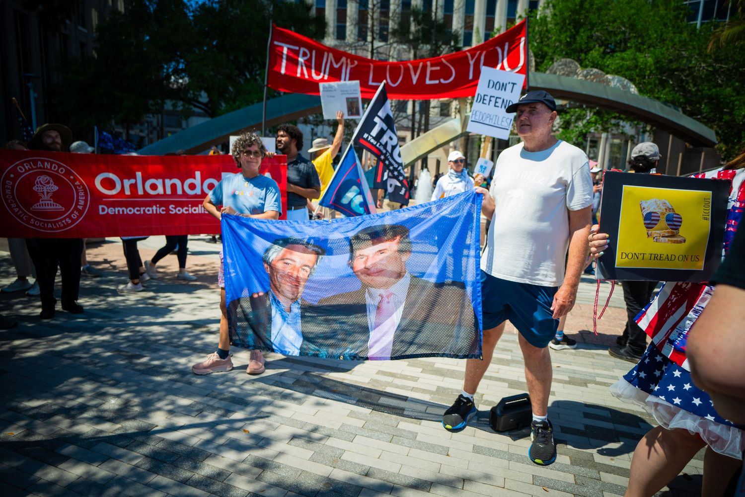 Protesters hold banners and flags during a political demonstration in downtown Orlando on a sunny day.