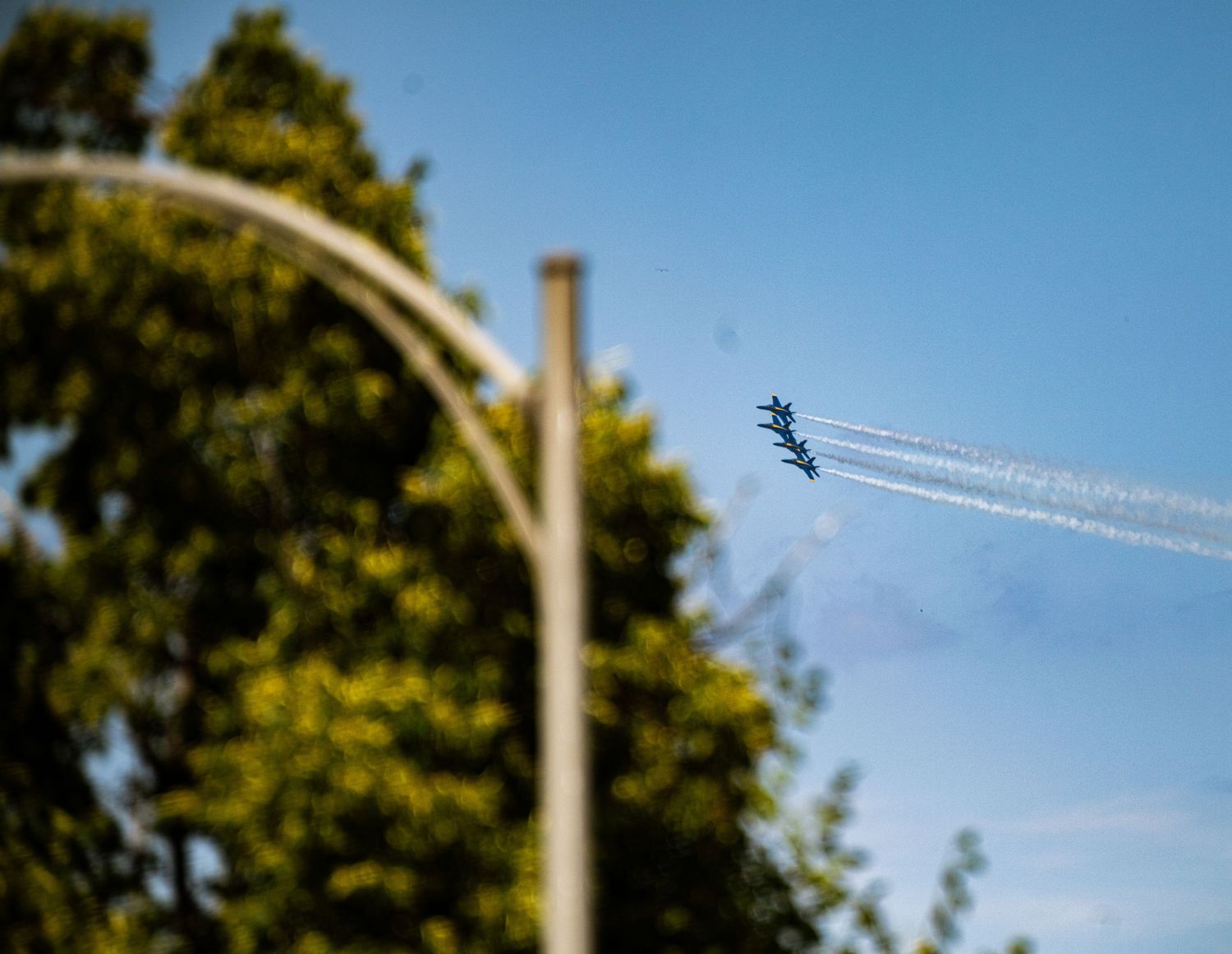 Military jets soar through bright blue skies leaving white contrails against a backdrop of trees.