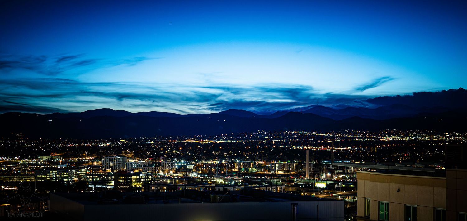 Panoramic cityscape of Reno Nevada at dusk with glowing lights and mountains silhouetted against a deep blue sky.