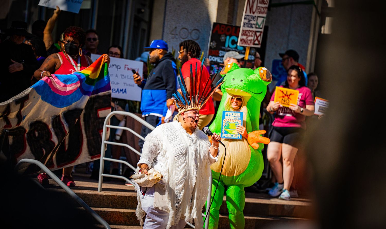 Colorful protest gathering with demonstrators in costumes and signs outside a building.