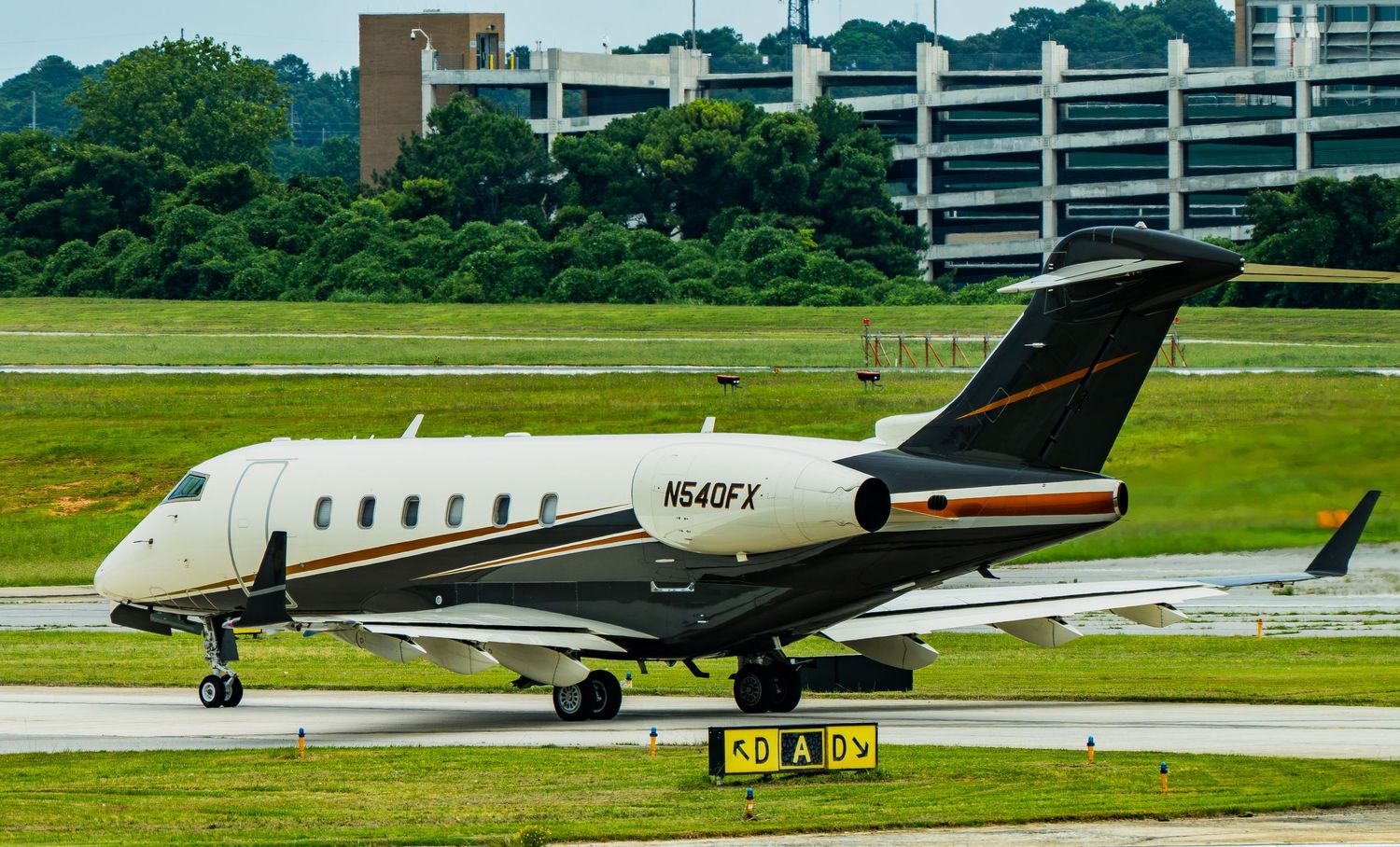 Private jet aircraft N549FX taxiing on runway at busy airport with green trees and buildings in background.