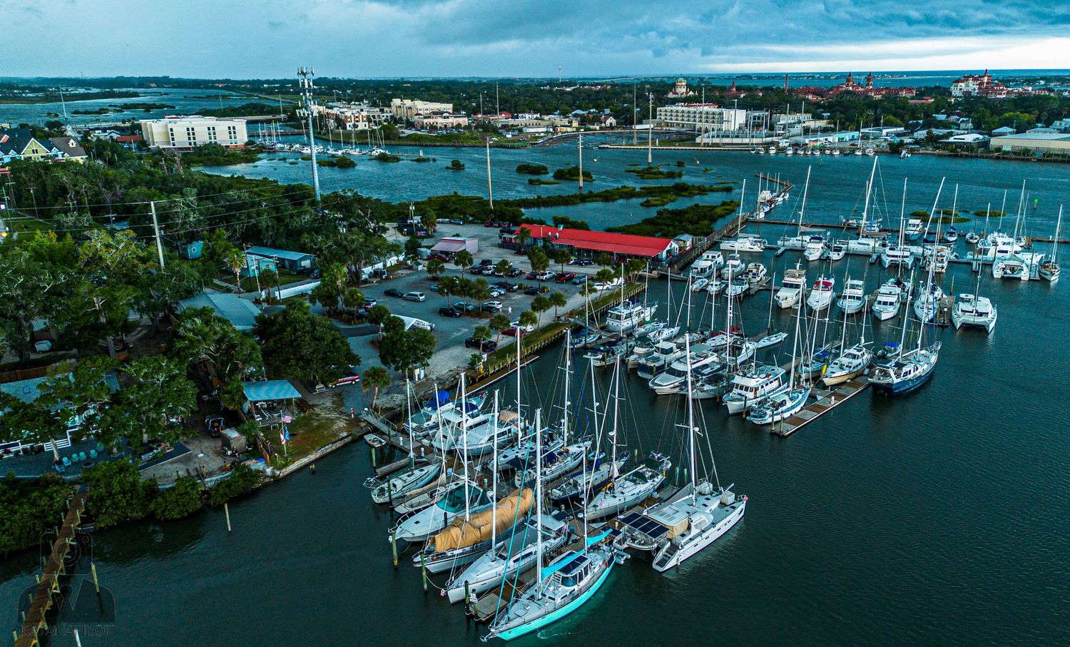 Aerial view of boats docked at a marina with blue water and cloudy skies.