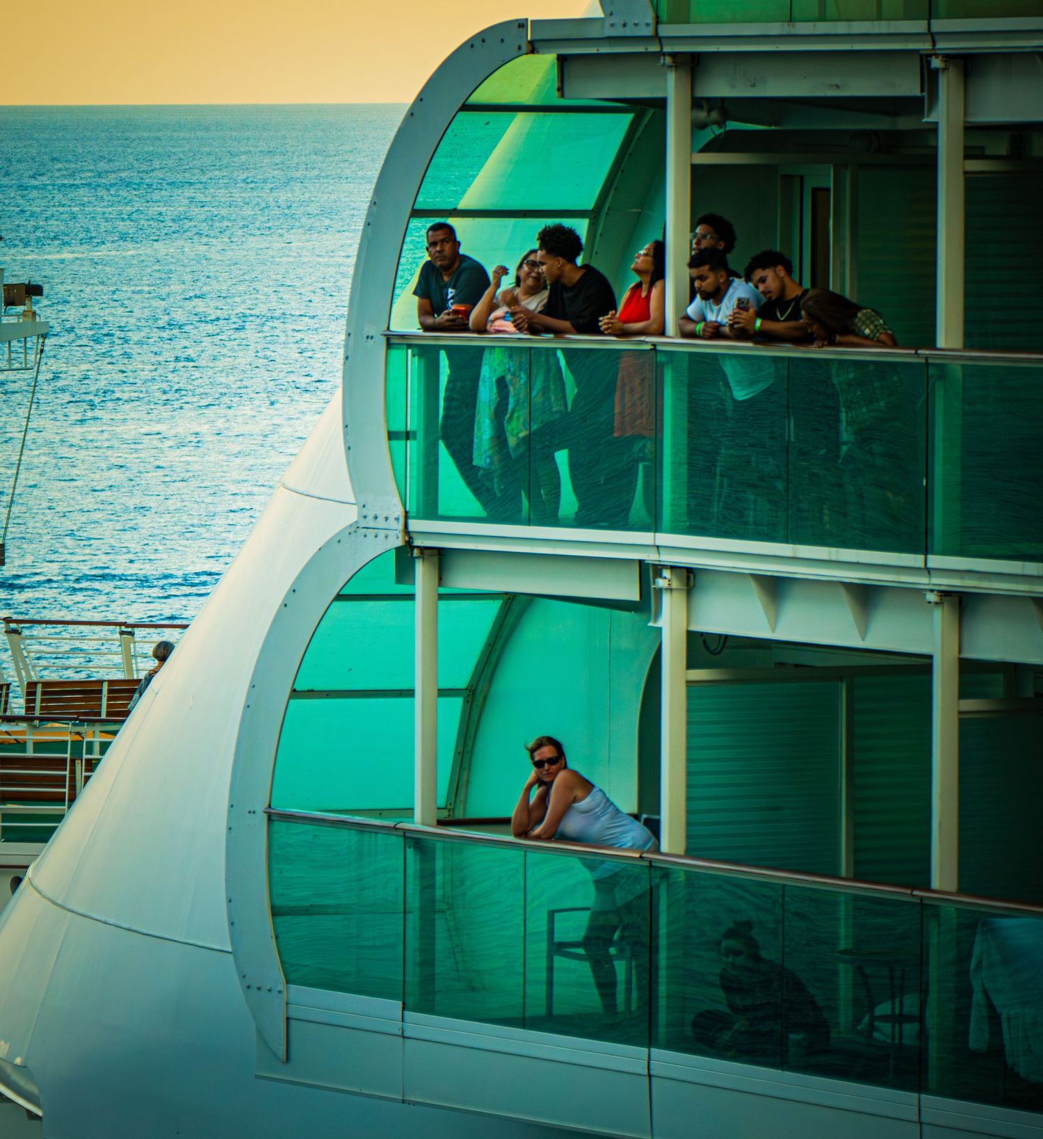 Cruise ship balconies in turquoise tint overlook calm ocean waters at sunset.