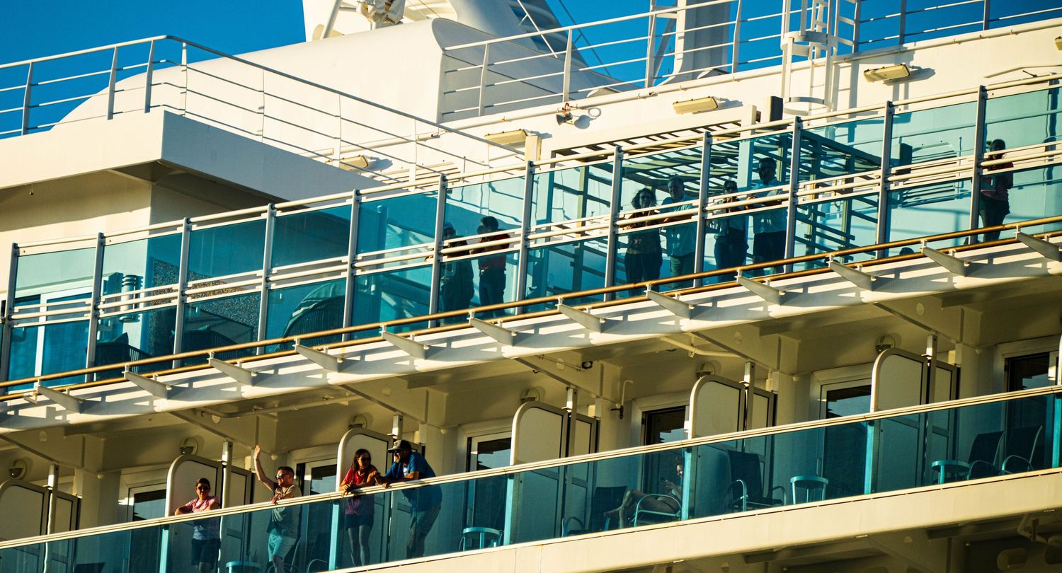 Balconies and railings on a luxury cruise ship deck against bright blue sky.