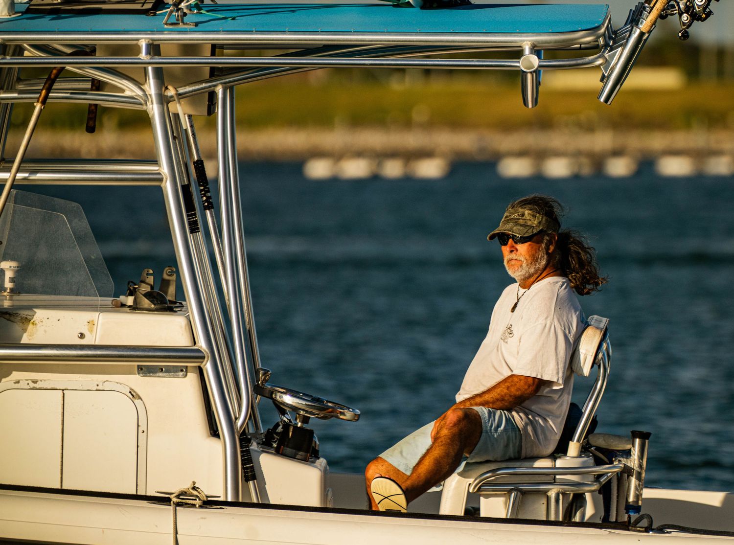 Person relaxing in captain's chair on boat with fishing gear and blue water in background on sunny day.
