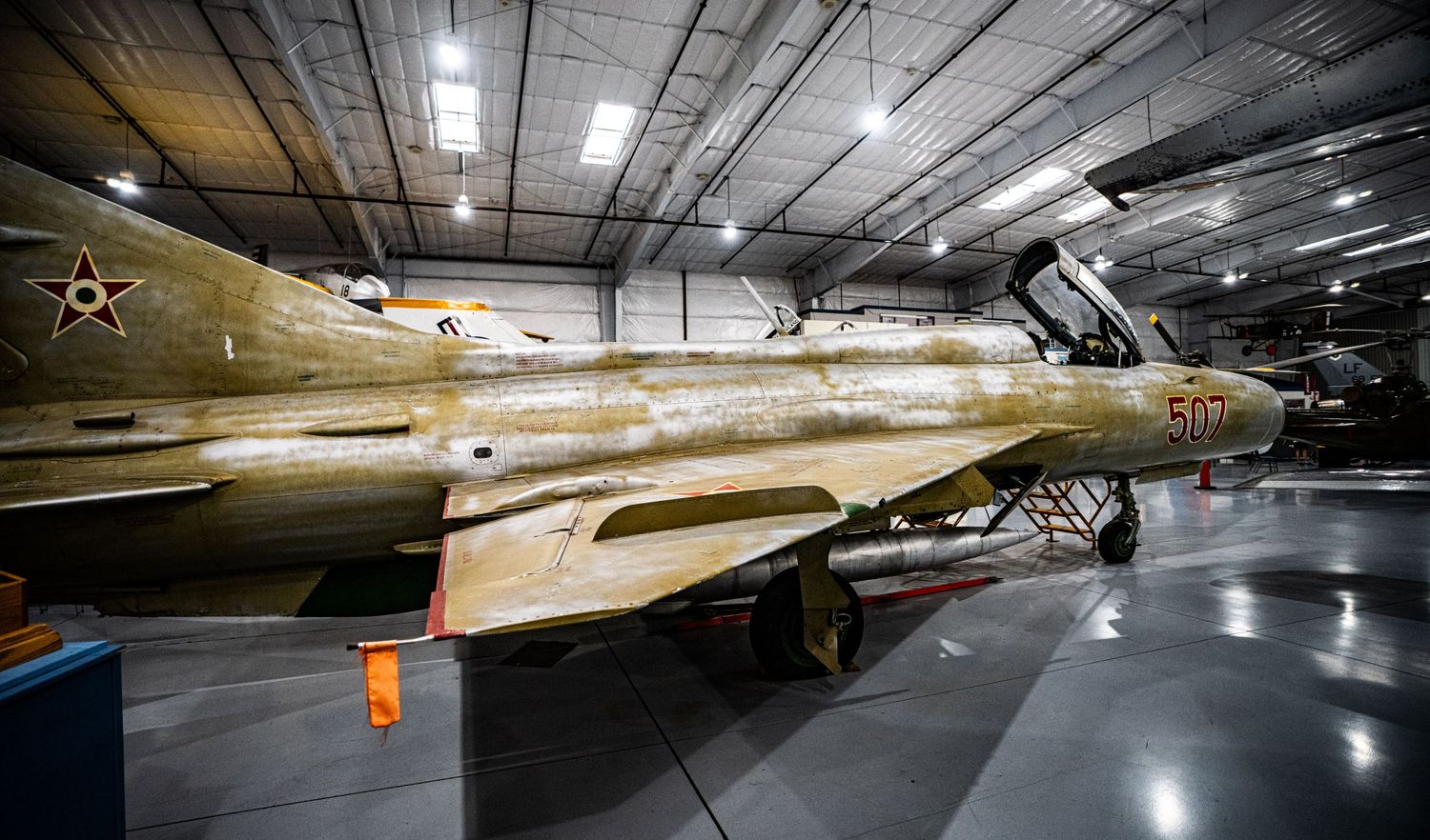 Vintage military jet fighter aircraft on display inside a museum hangar with desert camouflage paint scheme.