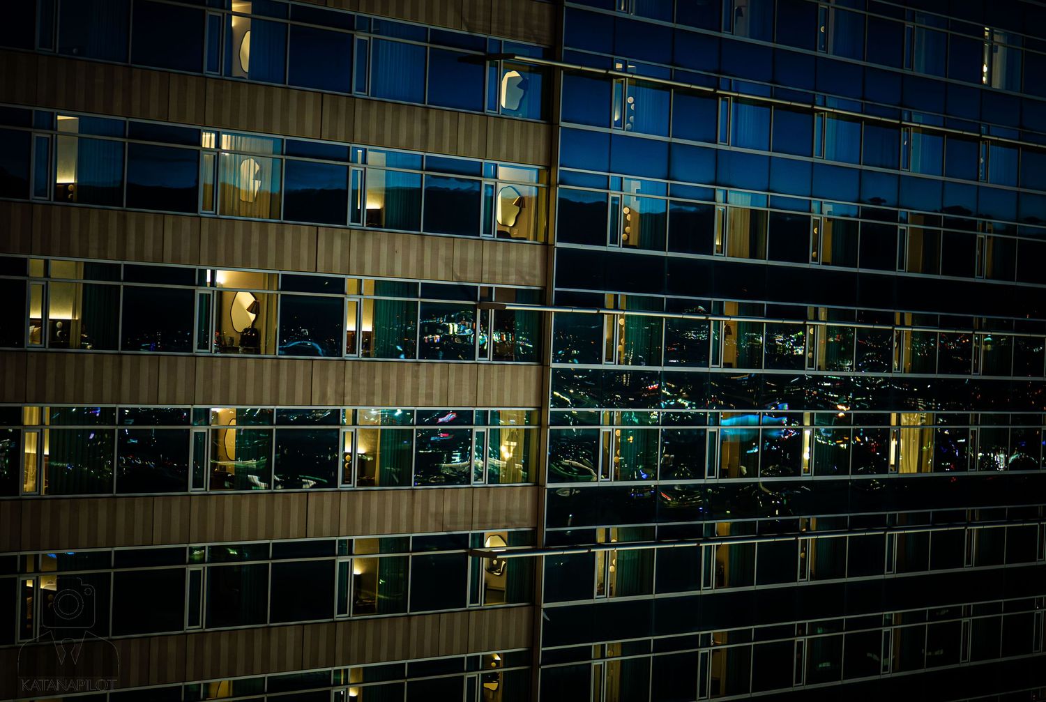 A modern office building exterior at night with illuminated windows creating a geometric pattern of light and shadow.