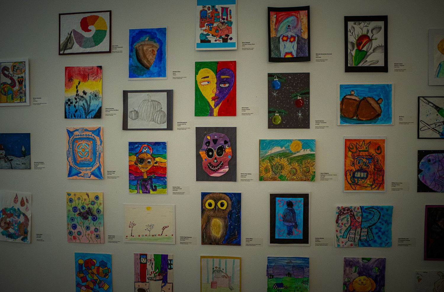 A wall gallery displays colorful children's artwork featuring various drawings and paintings in bright hues and whimsical styles.