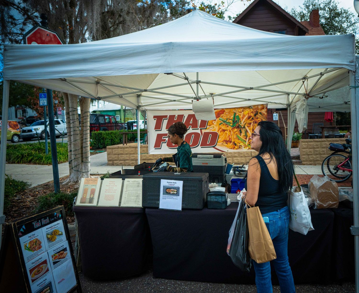 Outdoor market stalls with white canopy tents set up in a row selling various goods and food items.