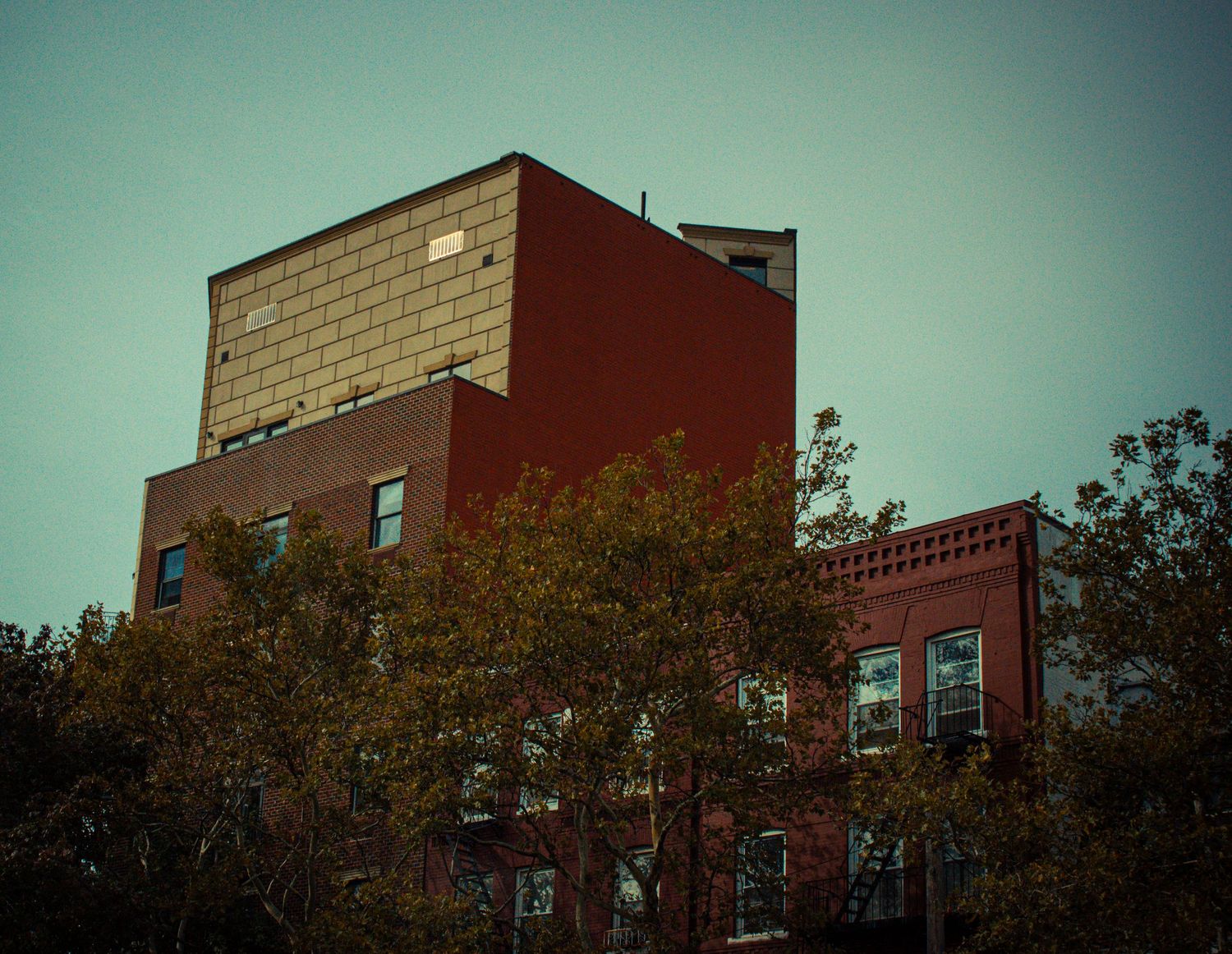 Red brick apartment buildings with trees line a residential street in an urban neighborhood.