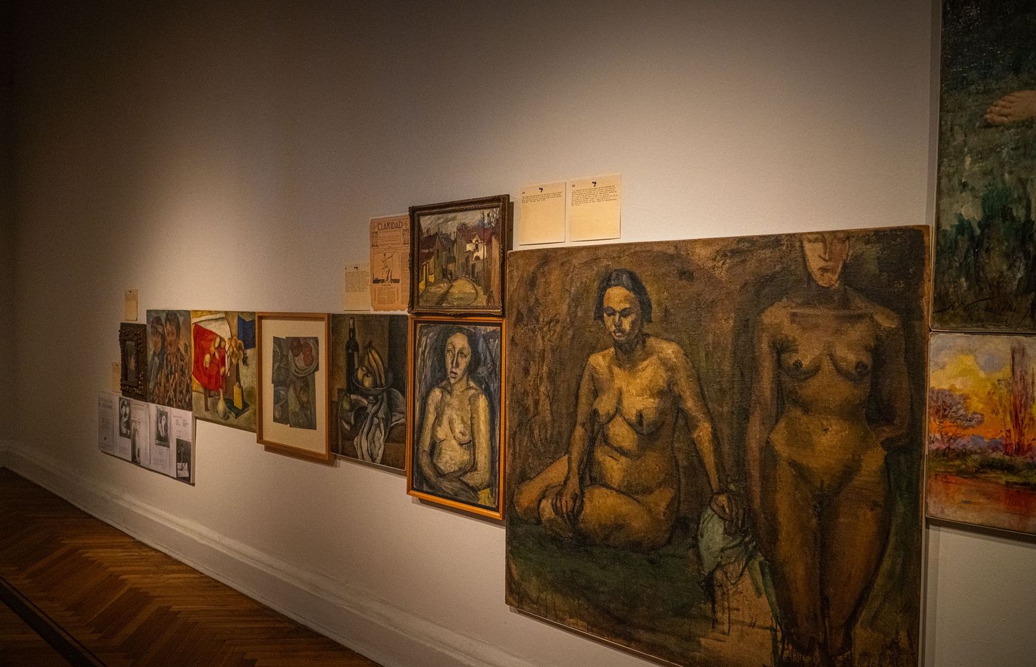 Gallery wall displaying a series of dark-toned portrait paintings in warm lighting.