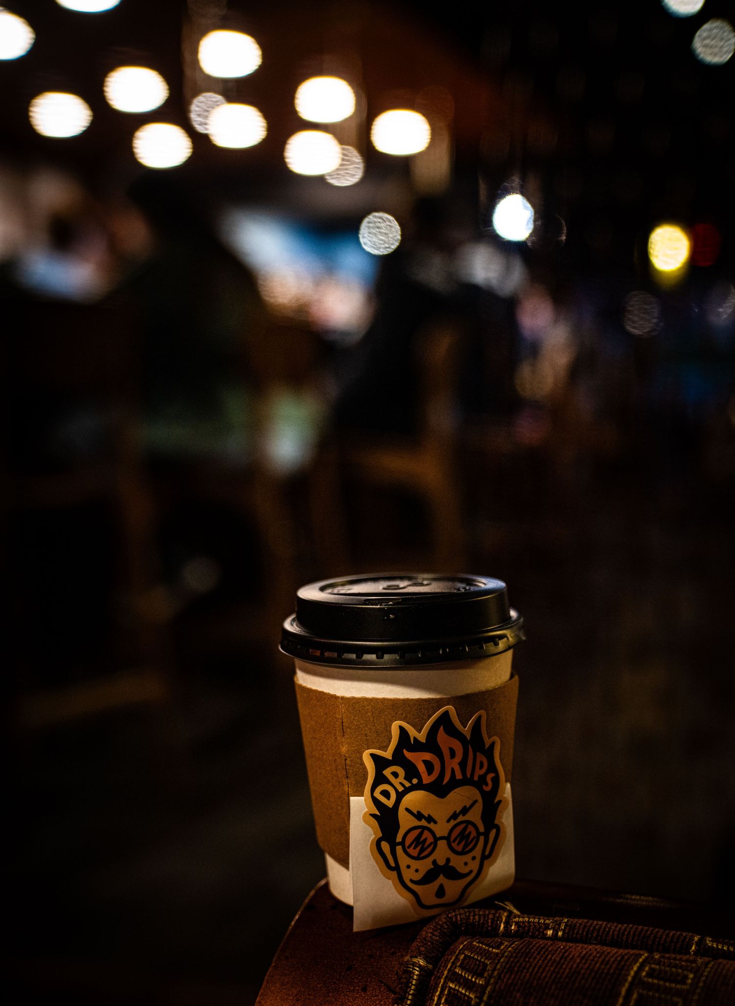 Blurred bokeh lights create an atmospheric backdrop behind a row of dark beer glasses in a dimly lit bar.