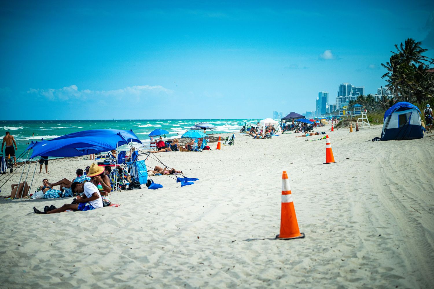 Beach scene with orange safety cones marking areas on pristine white sand near turquoise waters.