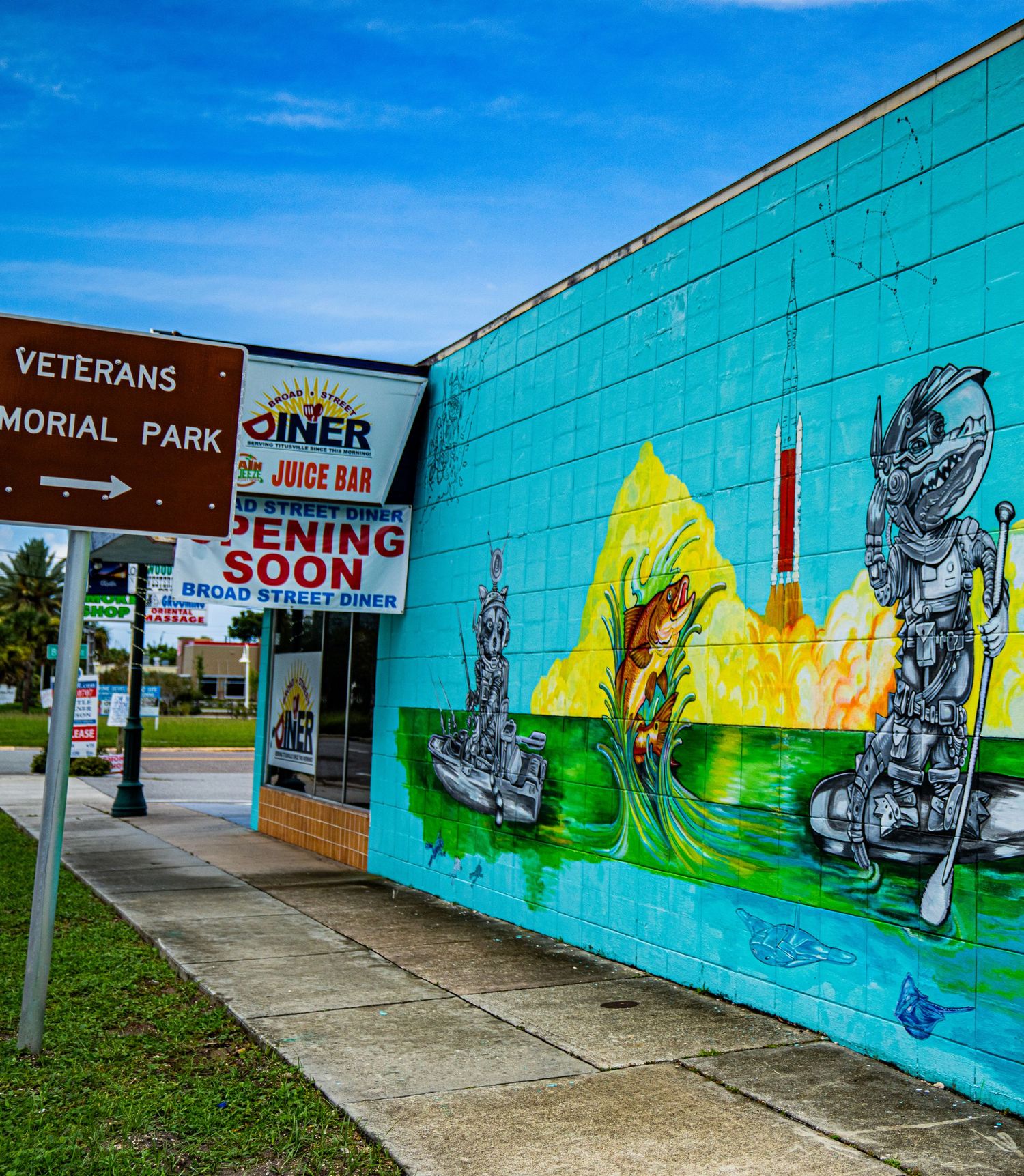 Turquoise building wall with street art near Veterans Memorial Park sign.