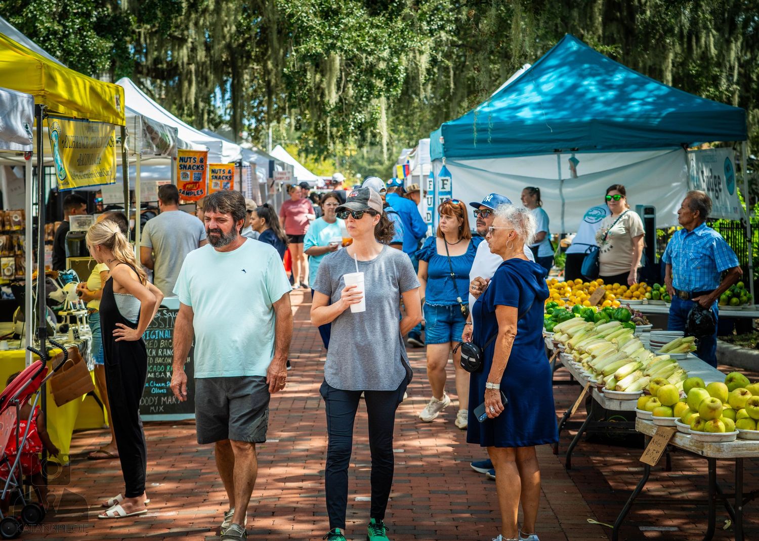 Farmers market walkway lined with vendor tents and shoppers browsing merchandise.