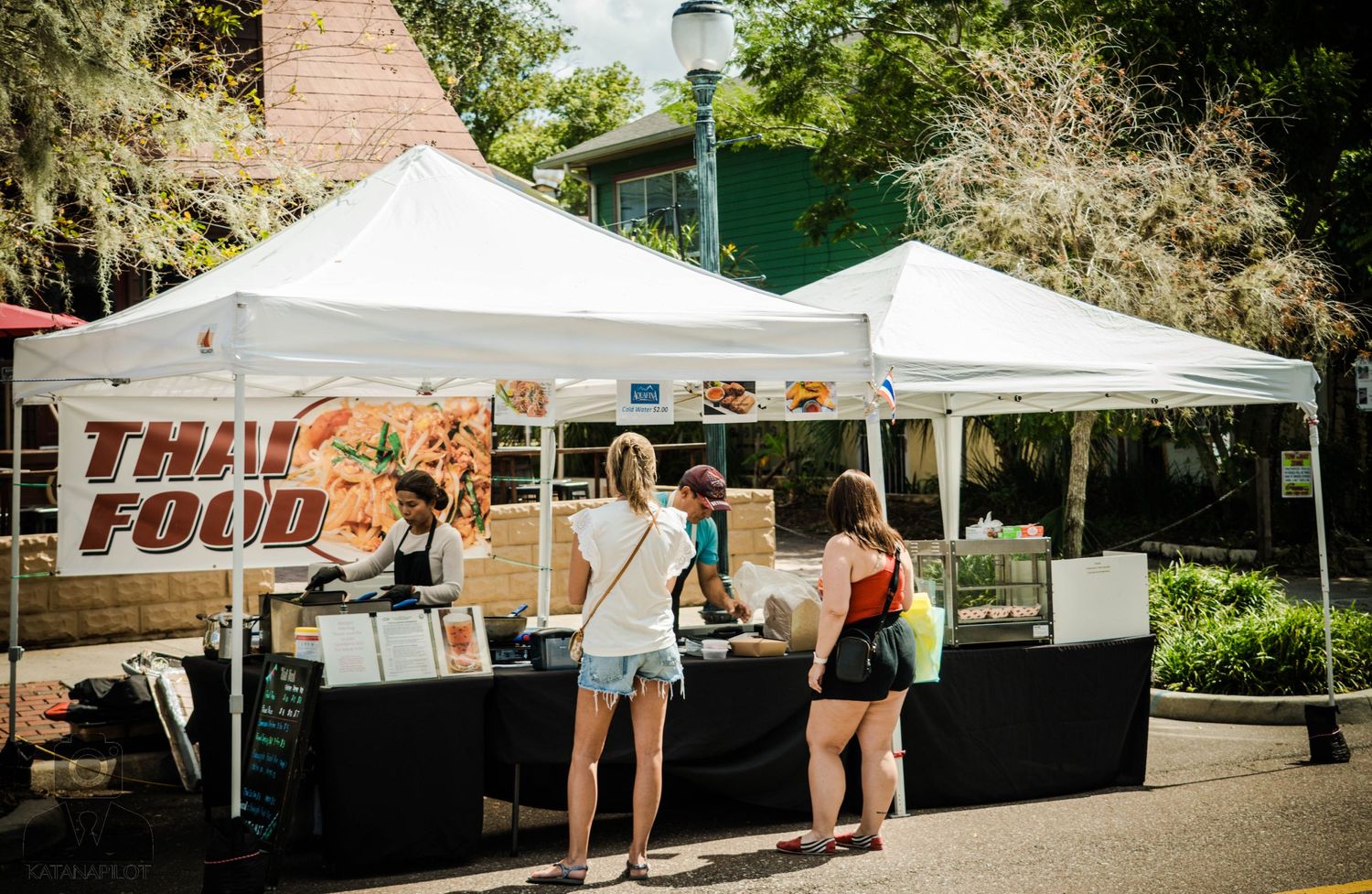 Thai food vendor booth with white tent canopy at outdoor market.