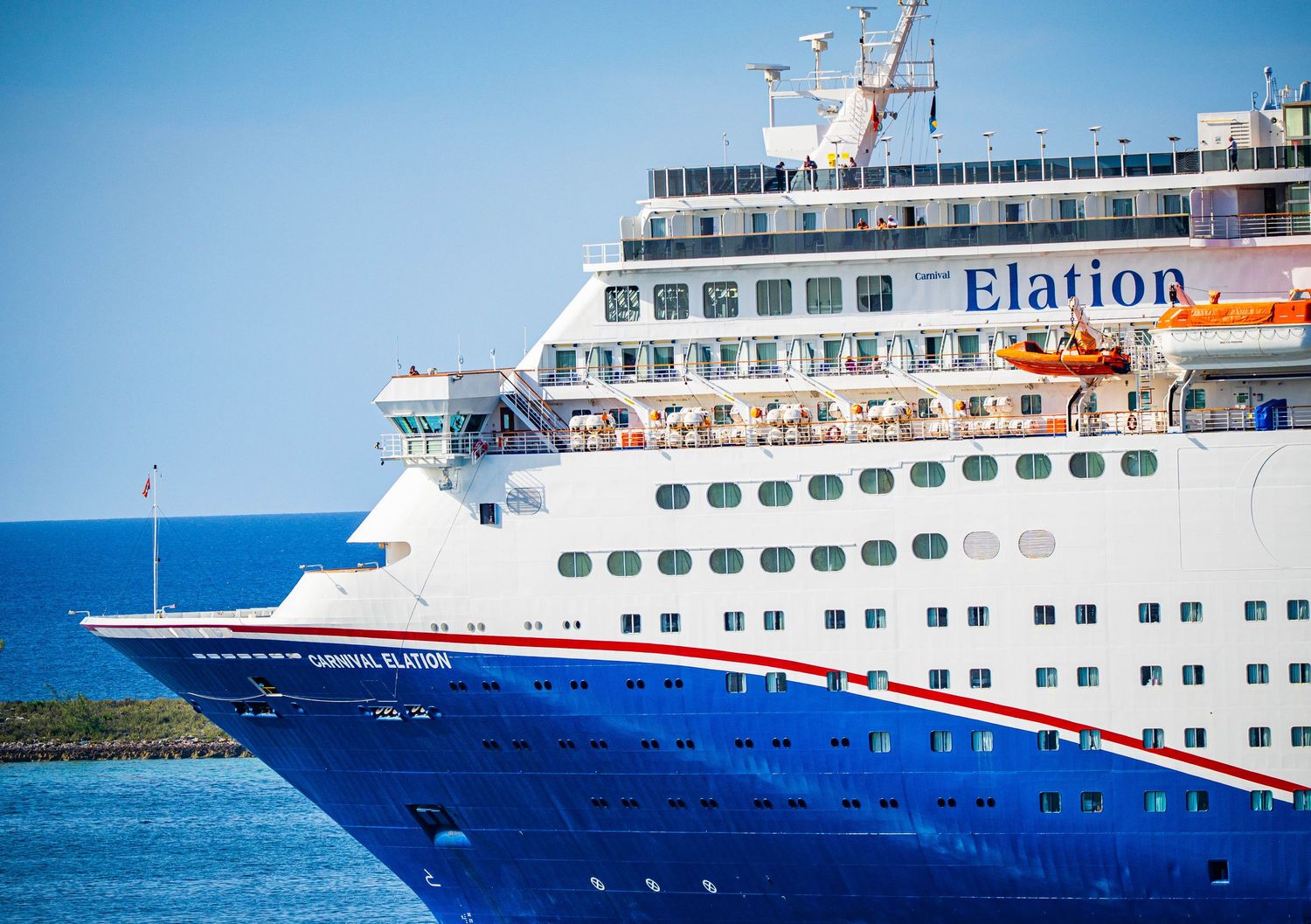Carnival Elation cruise ship sailing on blue ocean waters, showcasing its white hull and red stripe under clear skies.