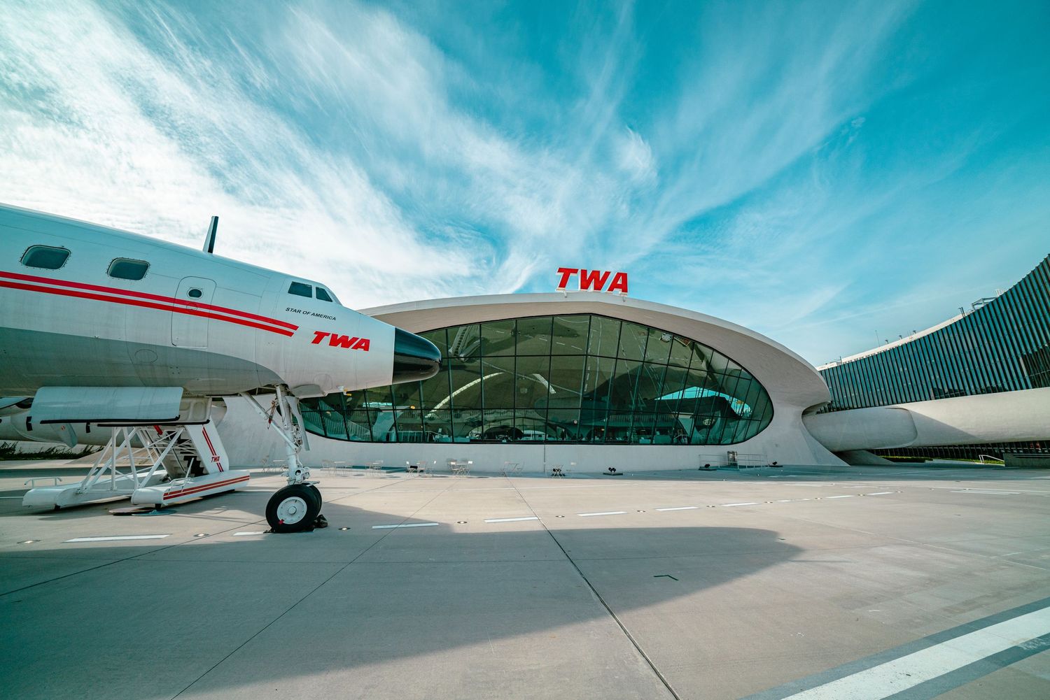 Private aircraft parked on tarmac under bright blue sky with dramatic clouds.