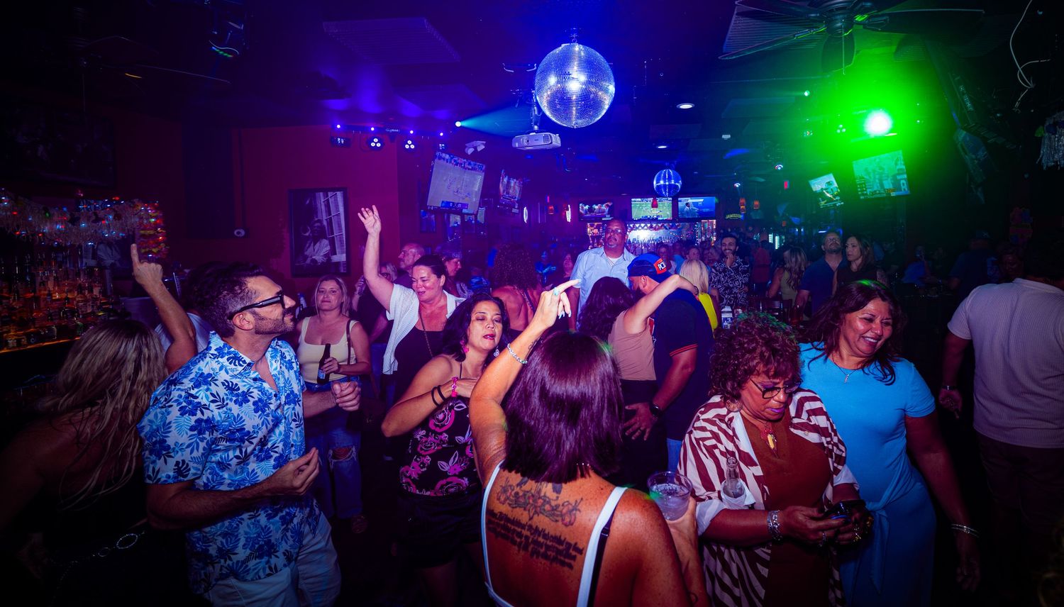 Crowded dance floor under disco ball with colorful lighting and energetic party atmosphere.