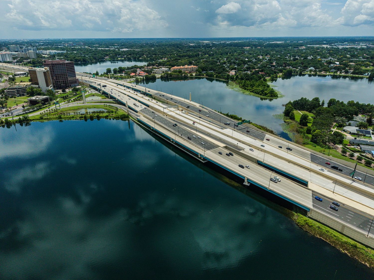Aerial view of a multi-lane highway bridge spanning a wide blue lake in an urban Florida cityscape.