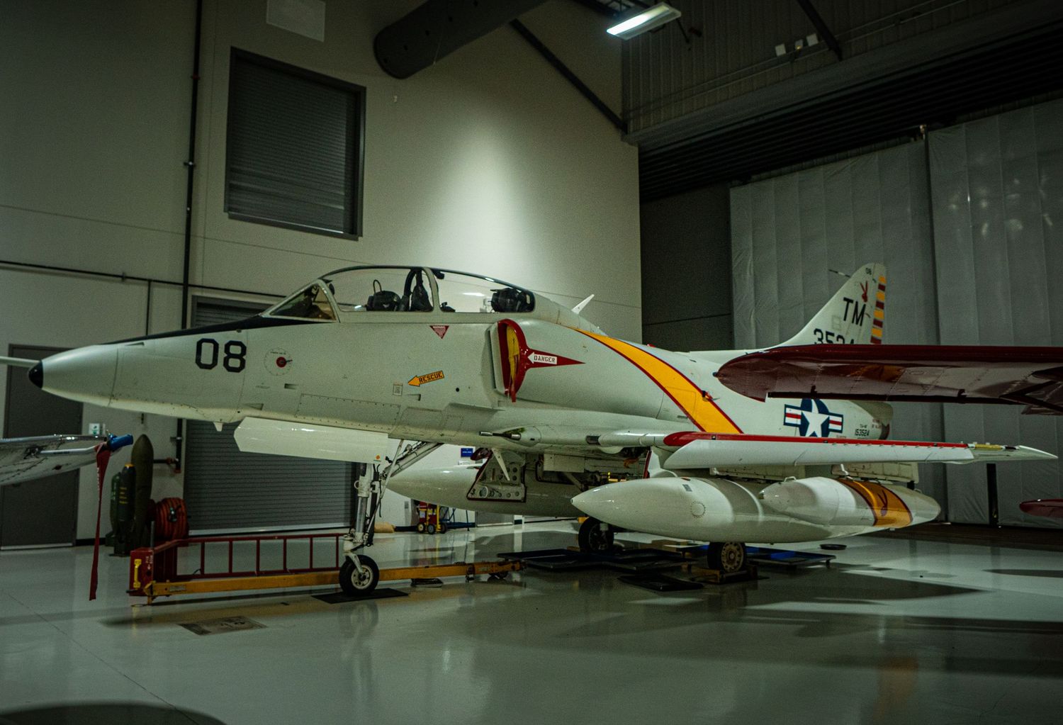 Navy jet fighter aircraft number 08 on display in a museum hangar with yellow and red markings.